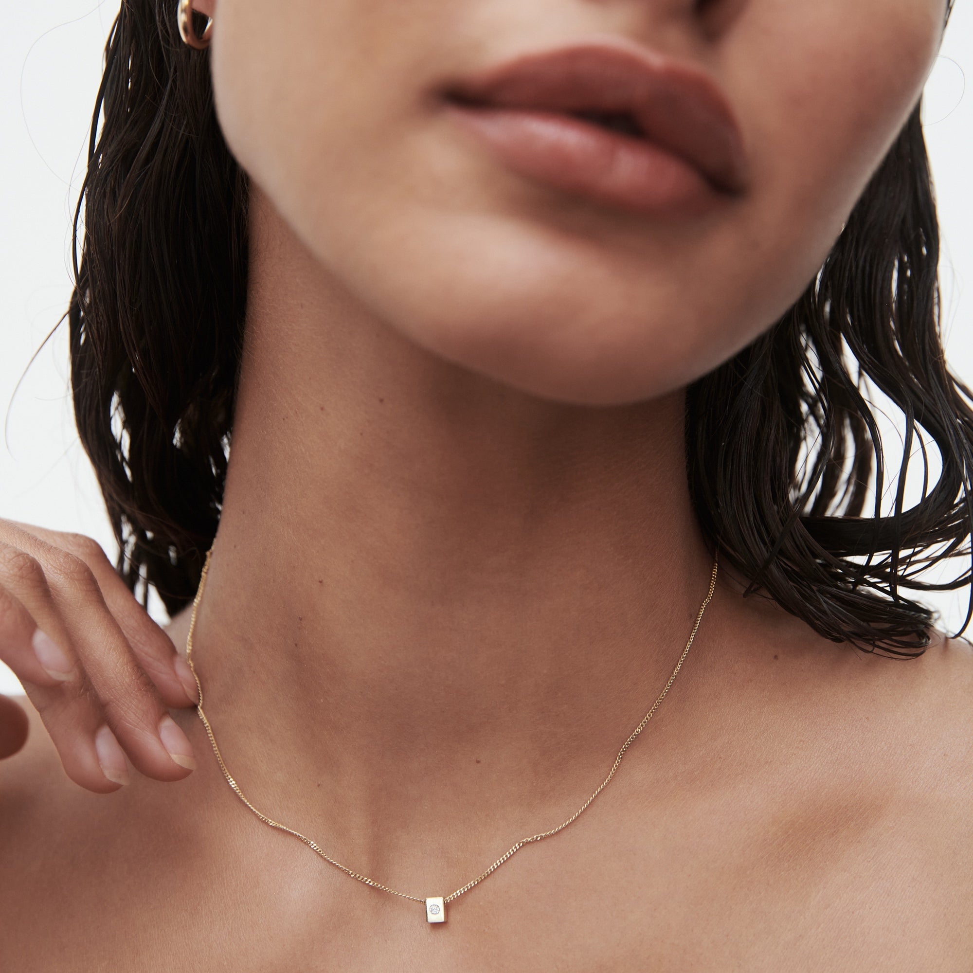 Close-up of a woman's neck wearing a minimalist gold necklace with a small rectangular pendant, highlighting luxury jewellery.