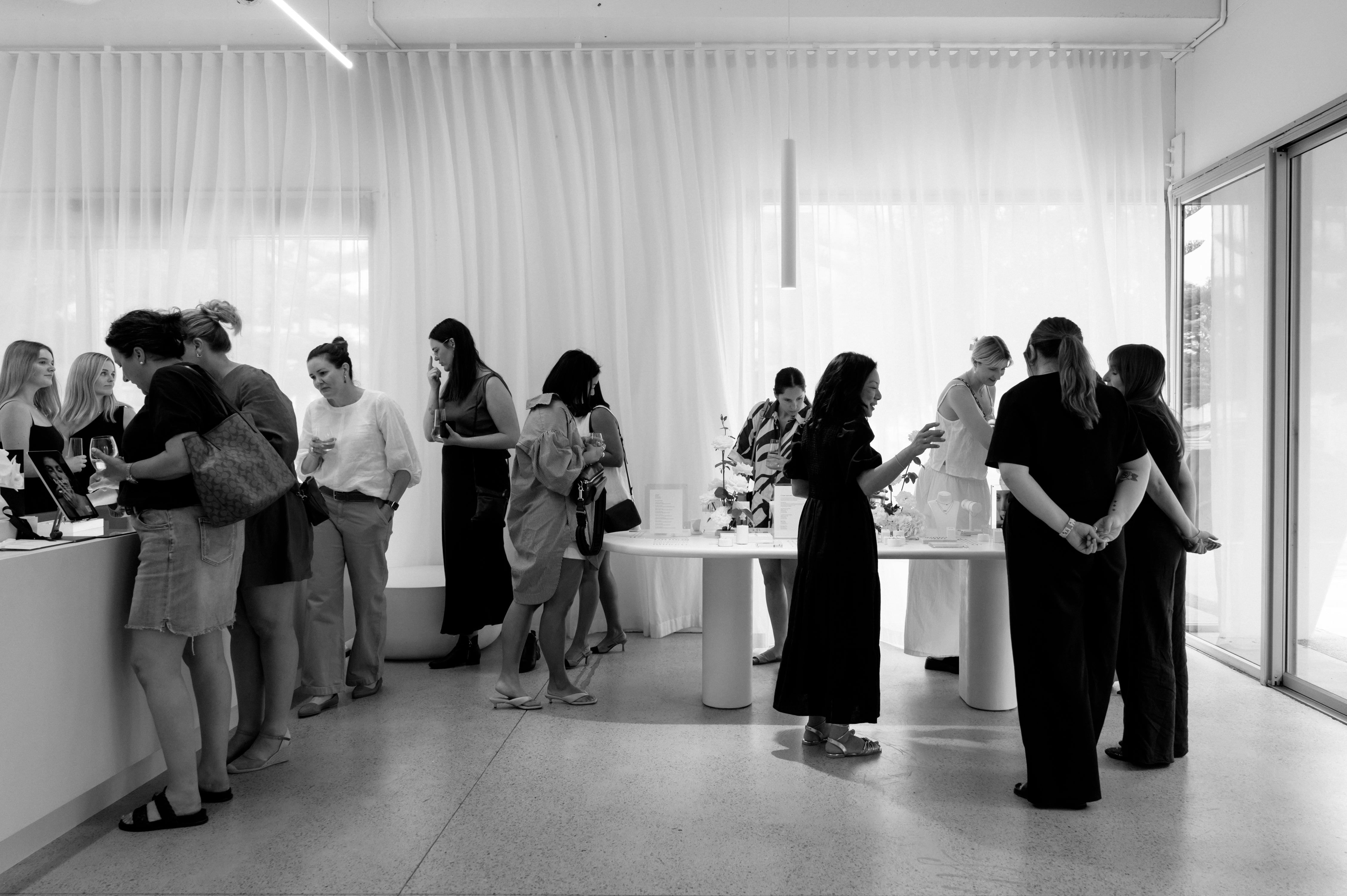 People in a modern jewellery store, browsing and discussing luxury items. Elegant decor with natural light and minimalist design.