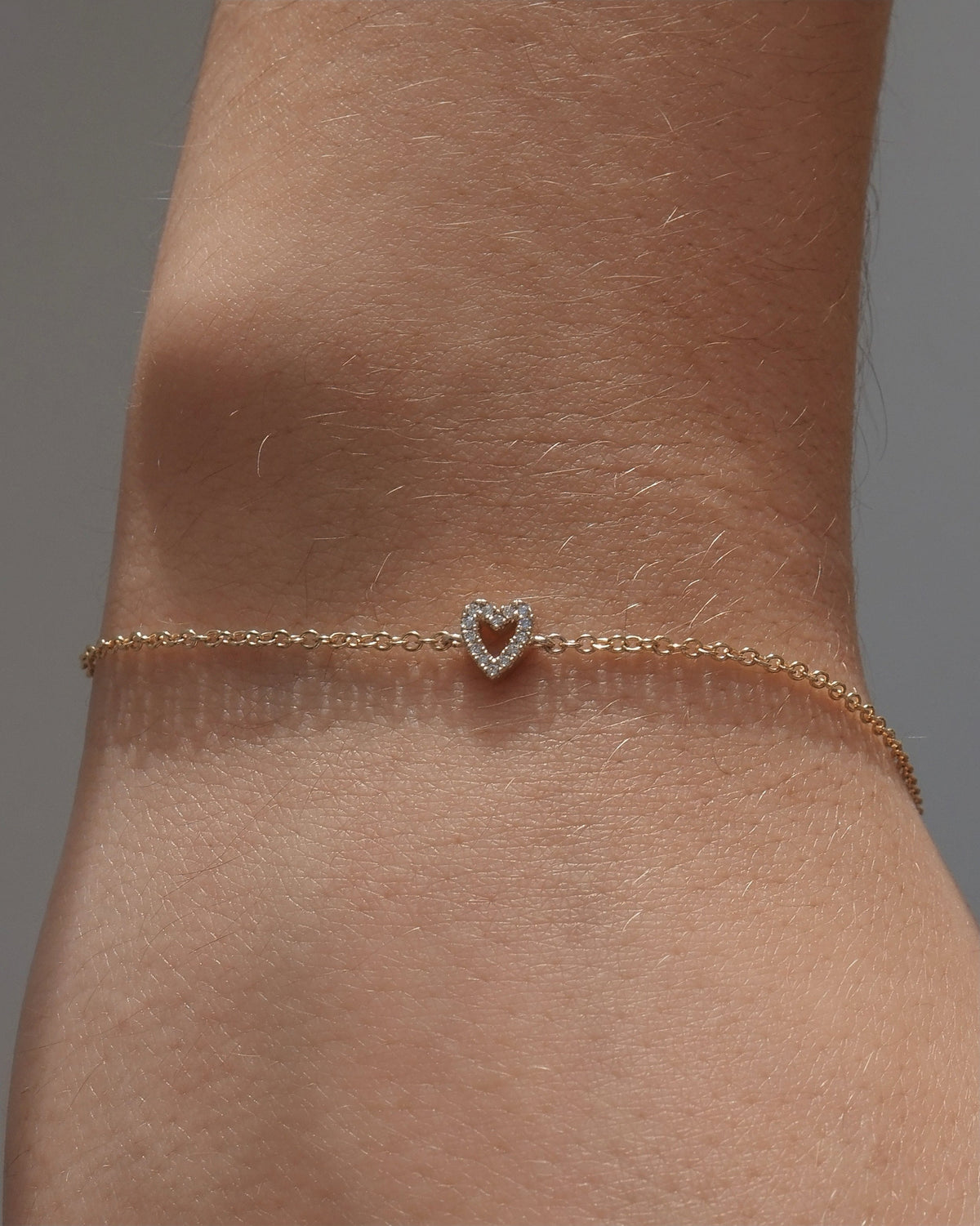 A delicate gold chain bracelet with a small heart-shaped lab grown diamond charm, shown worn on a person's wrist.