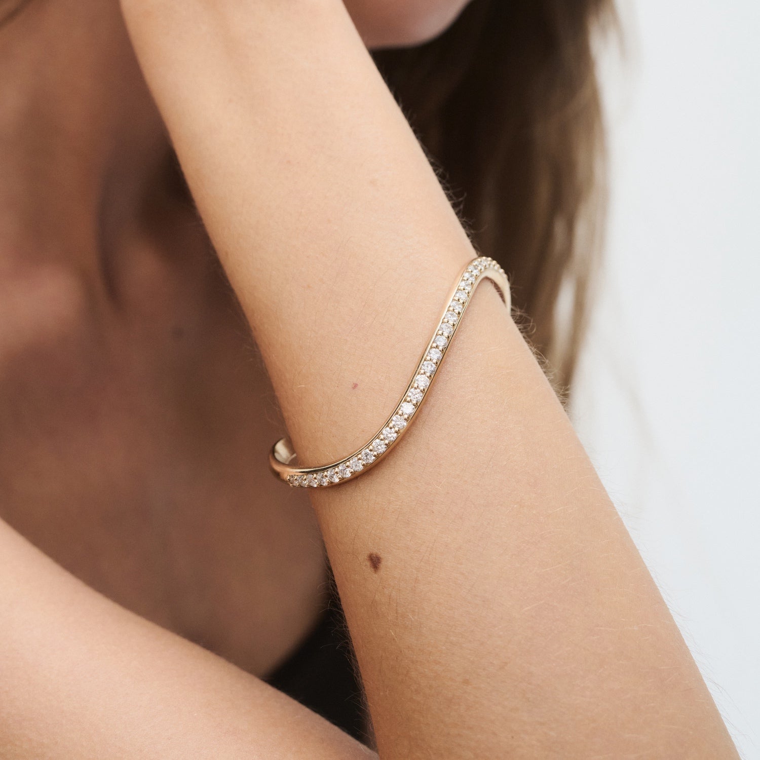Woman wearing an elegant diamond-studded gold bangle on her wrist, showcasing luxury jewellery style against a simple backdrop.