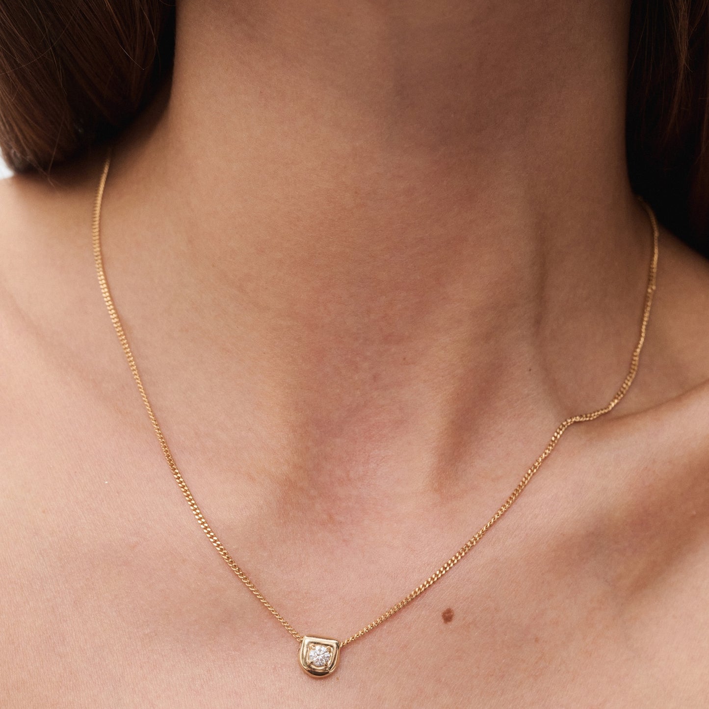 Elegant gold necklace with a small, square diamond pendant, worn on a woman's neck. Luxury jewellery, minimalist design.
