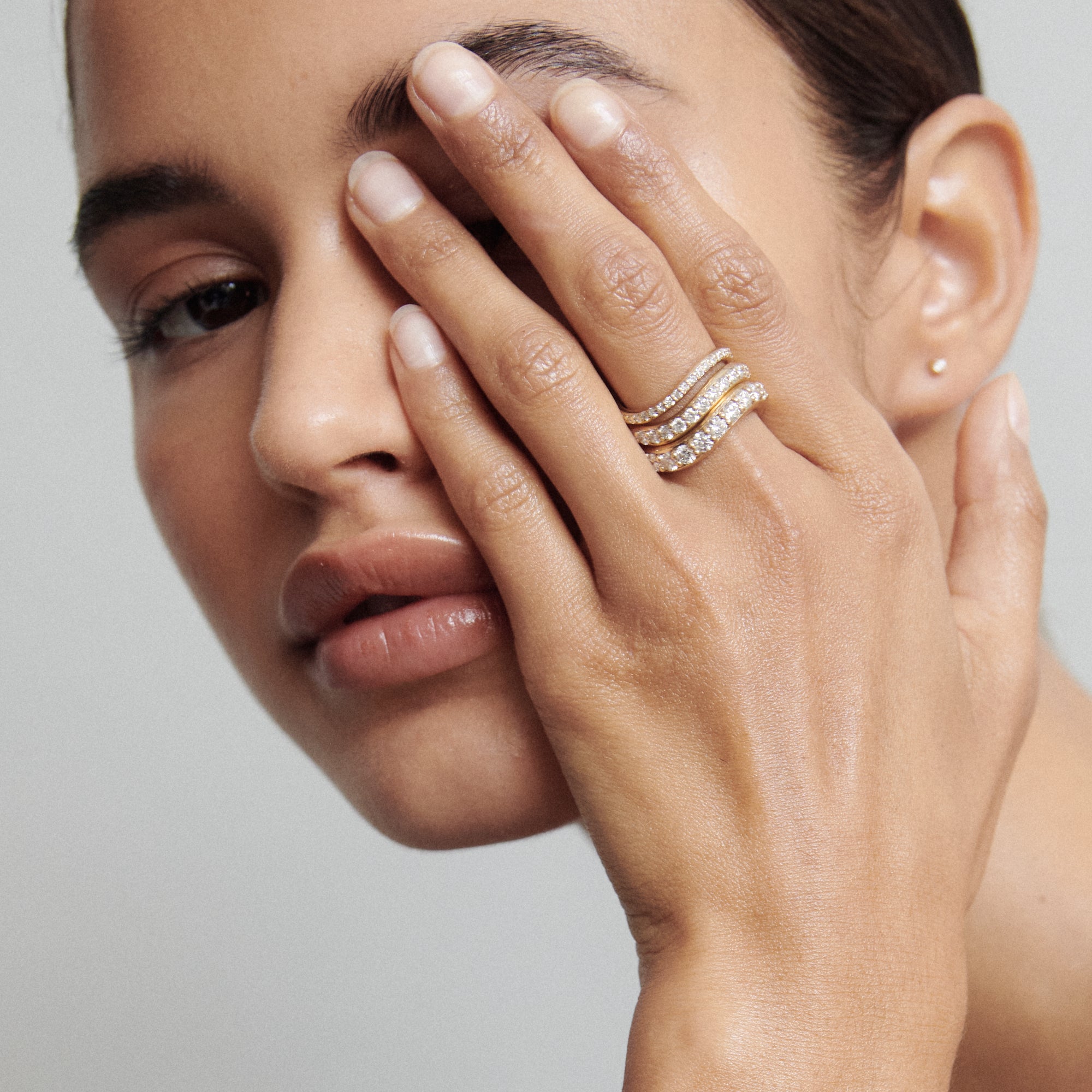 Woman showcasing gold and diamond rings on her fingers, covering half of her face. Elegant and luxurious jewellery display. [text overlay:] 