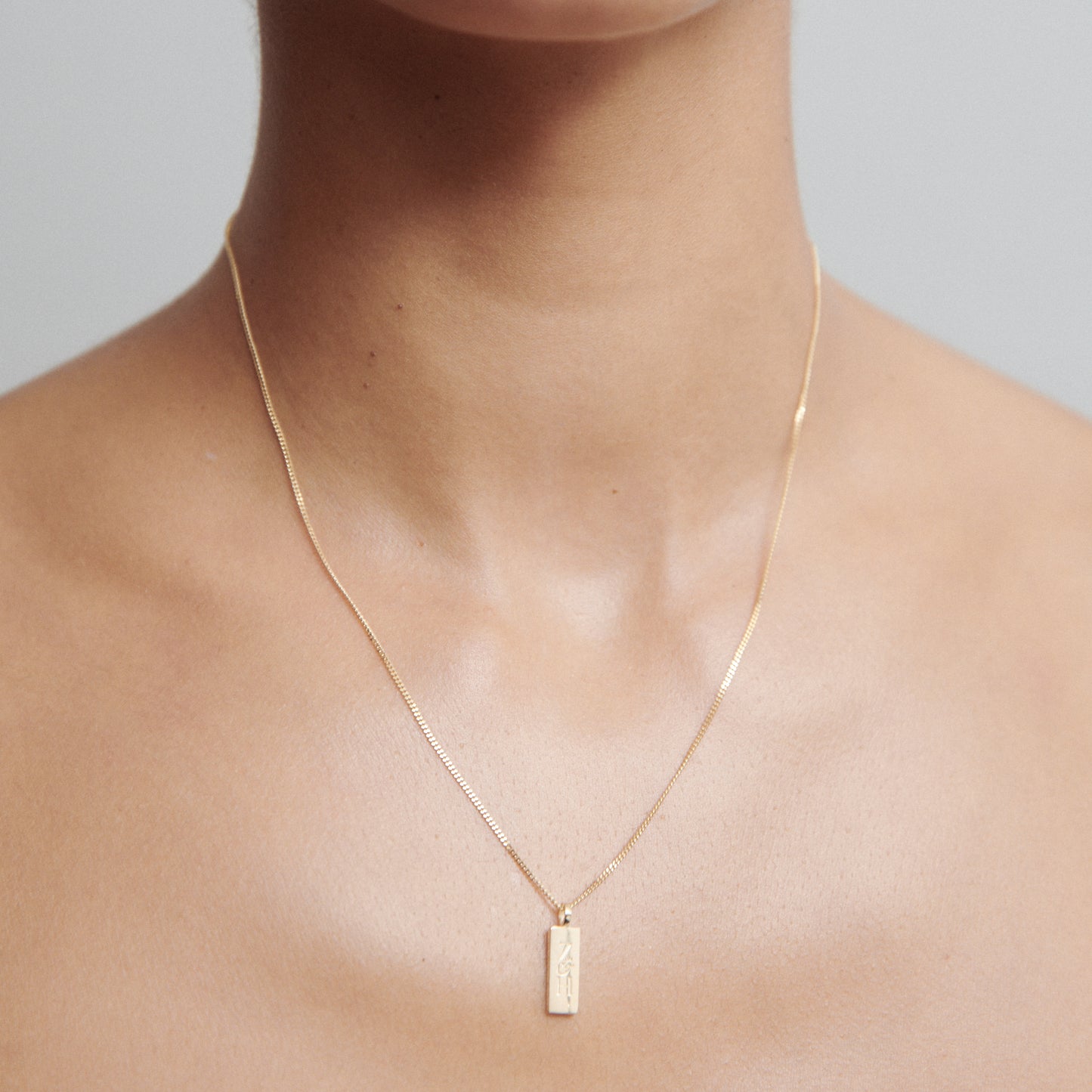 Minimalist gold necklace with a rectangular pendant on a model's neck, showcasing luxury jewellery design and elegance.