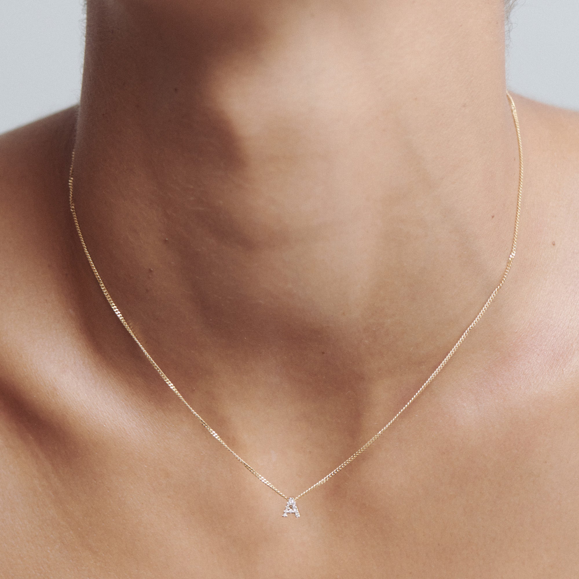 Elegant gold necklace with a small triangle-shaped diamond pendant on a woman's neck. Luxury jewellery, minimalist design.