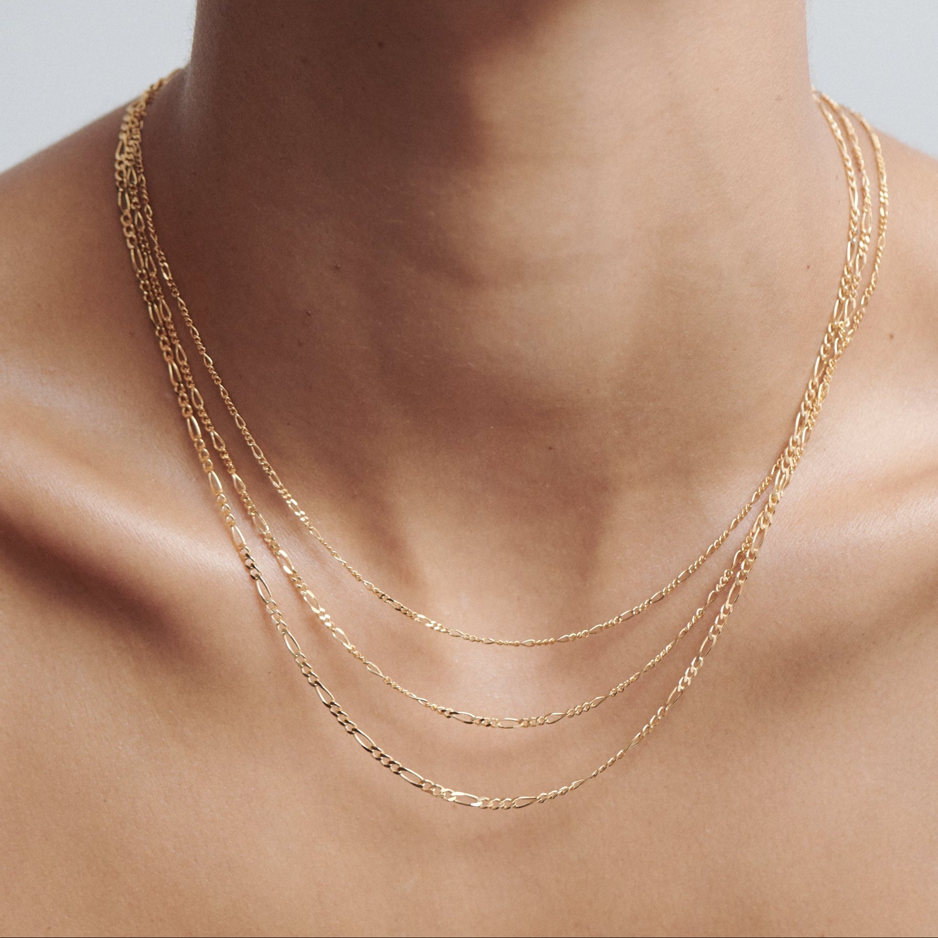 Close-up of a person wearing three delicate gold chains layered elegantly around the neck, showcasing luxury jewellery fashion.