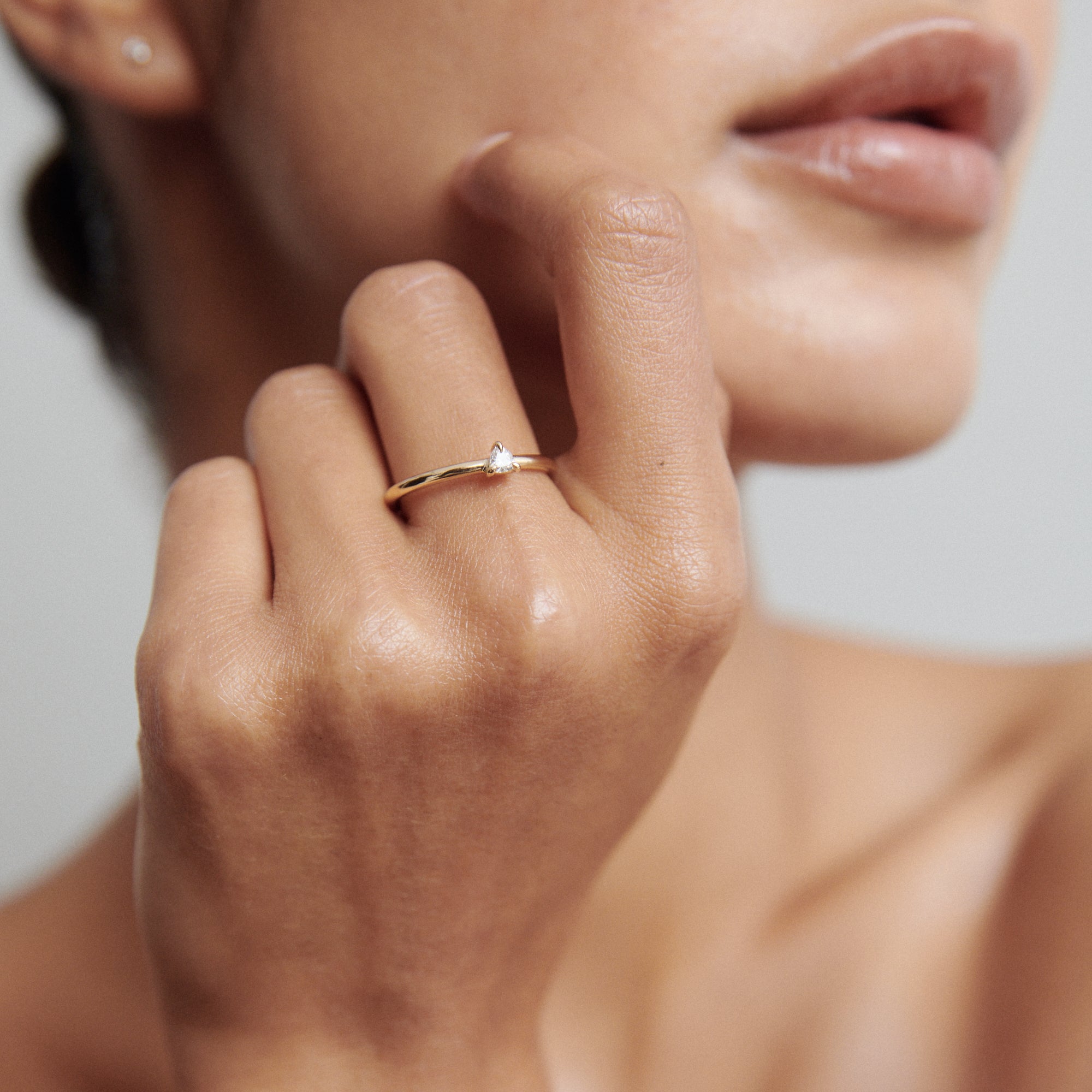 Woman's hand near face wearing a delicate gold ring with a small diamond. Luxurious jewellery showcased against soft skin tones.