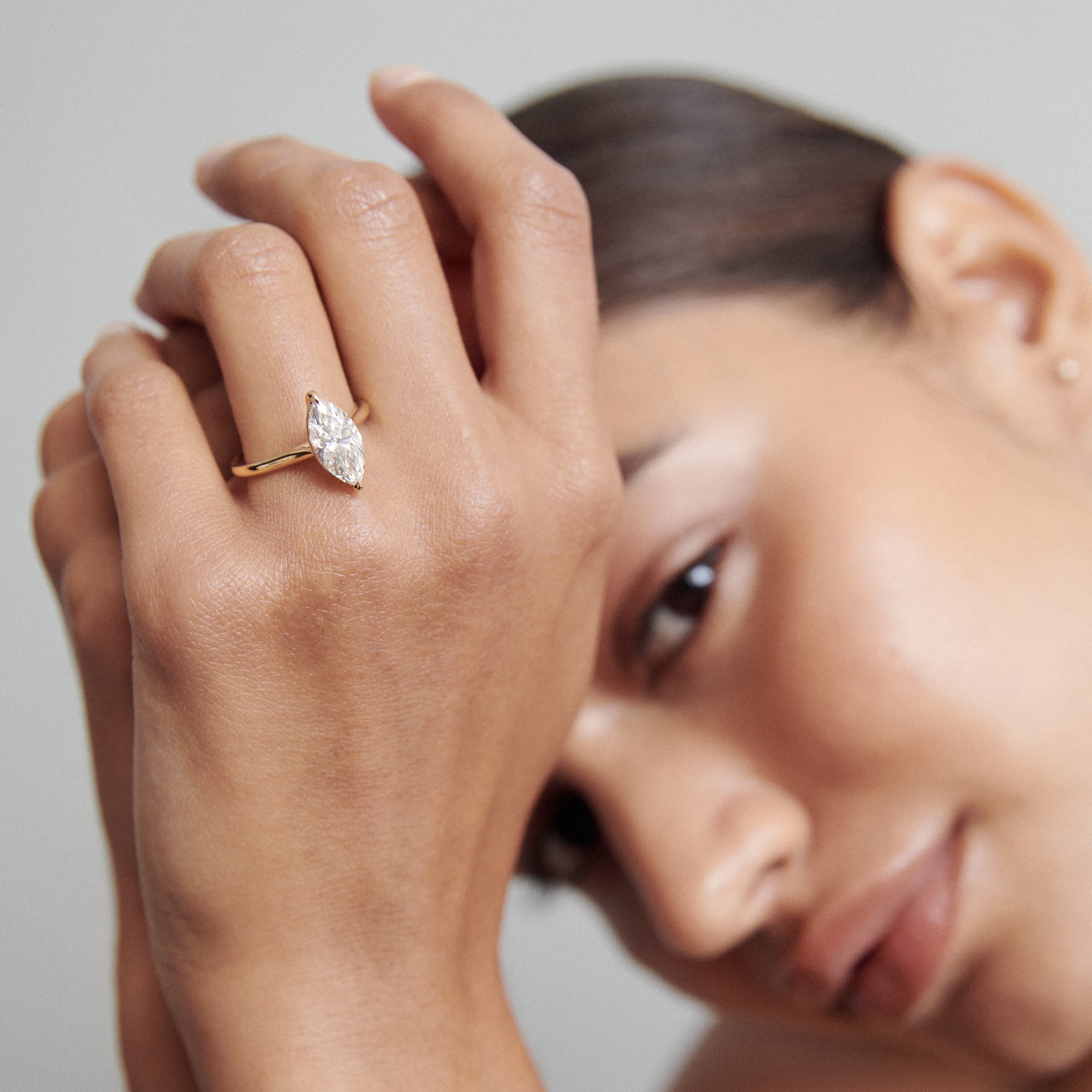 Woman showcasing an elegant marquise-cut diamond ring on her hand, with a soft focus on her serene expression, highlighting luxury jewellery.
