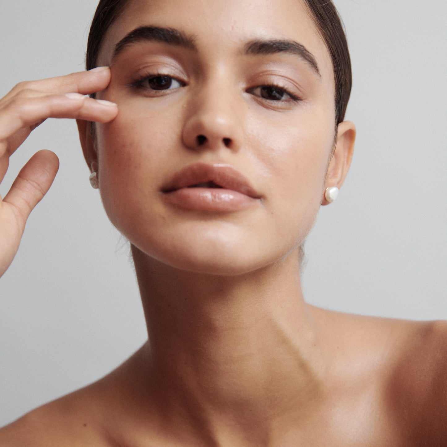 Woman wearing elegant pearl earrings, with minimal makeup and sleek hairstyle, gazing softly. Luxurious jewellery focus.