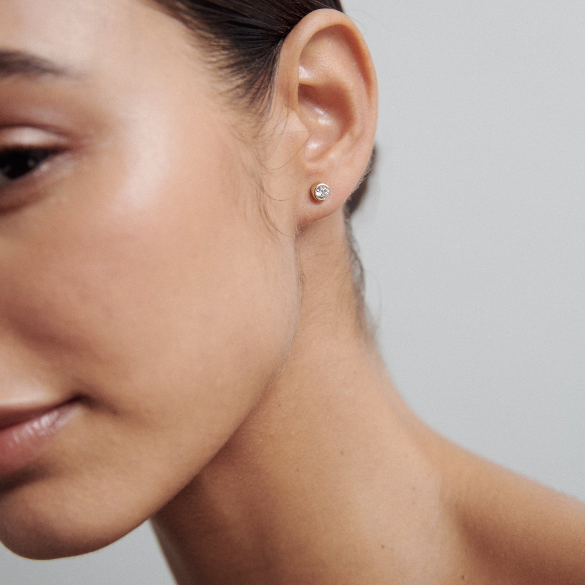 Close-up of a woman's ear wearing a single diamond stud earring. The focus is on the jewellery, highlighting its simplicity and elegance.