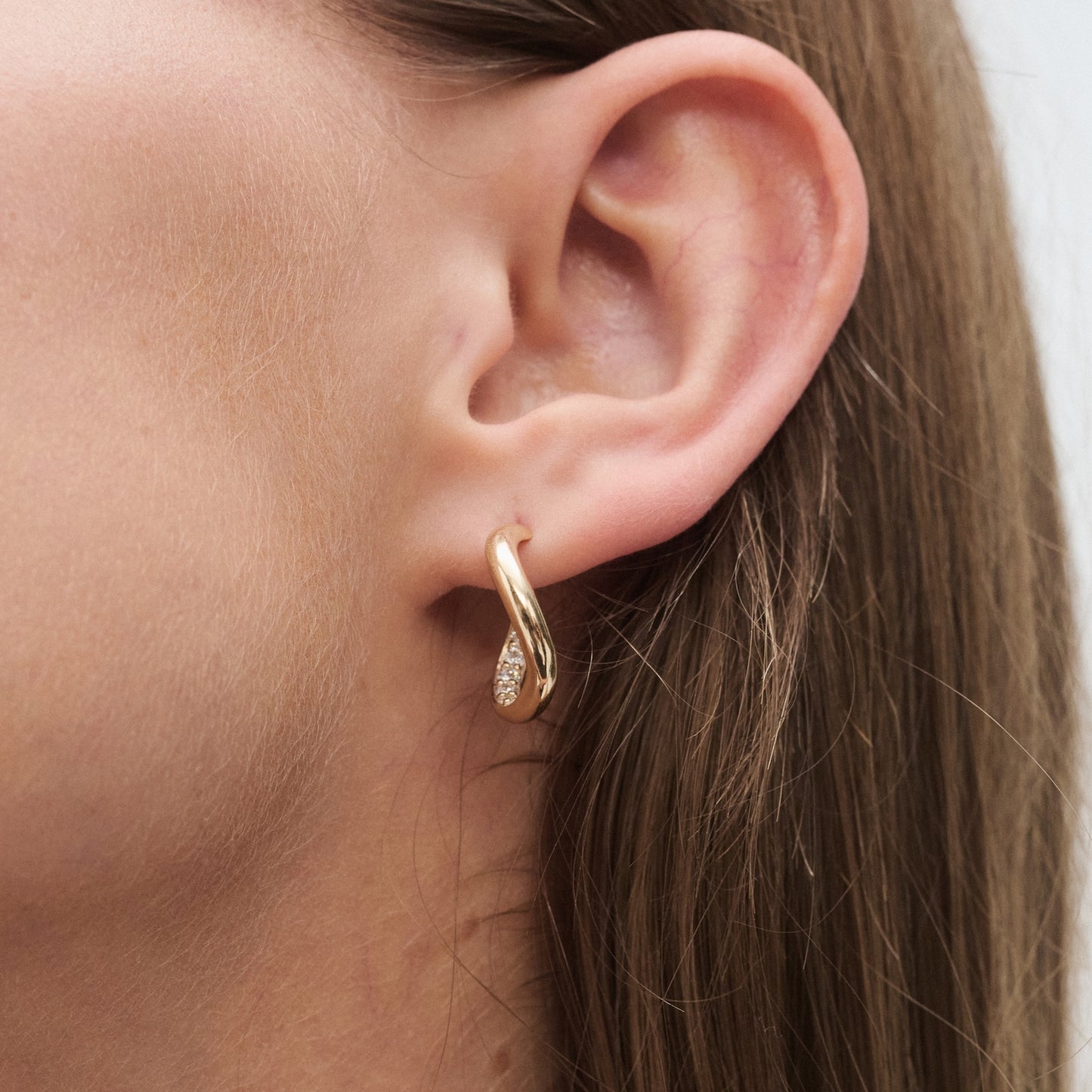 Close-up of a woman's ear wearing a gold hoop earring with a small teardrop diamond pendant, showcasing luxury jewellery.