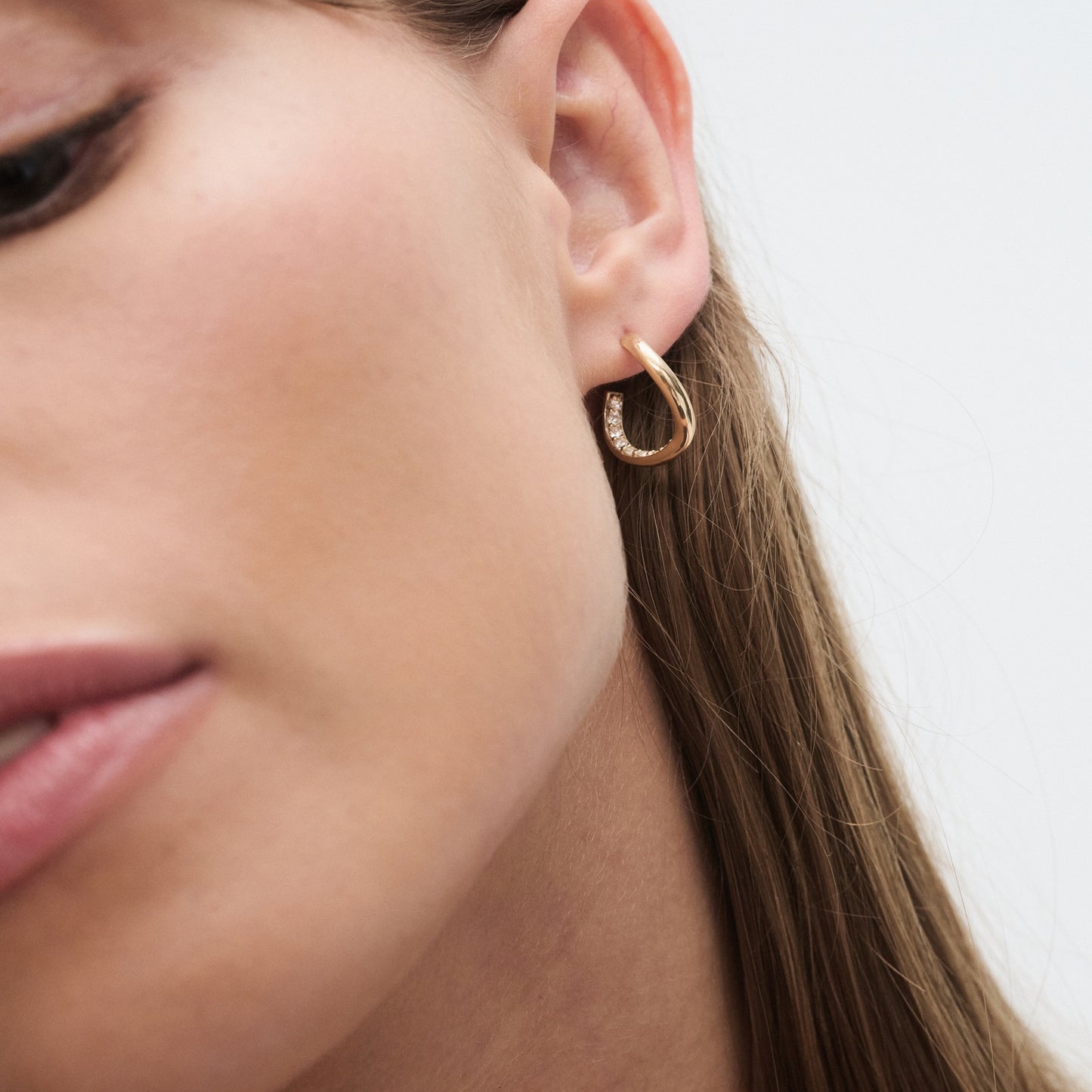 Close-up of a woman's ear adorned with a small, elegant gold hoop earring featuring delicate diamond accents. Luxury jewellery.