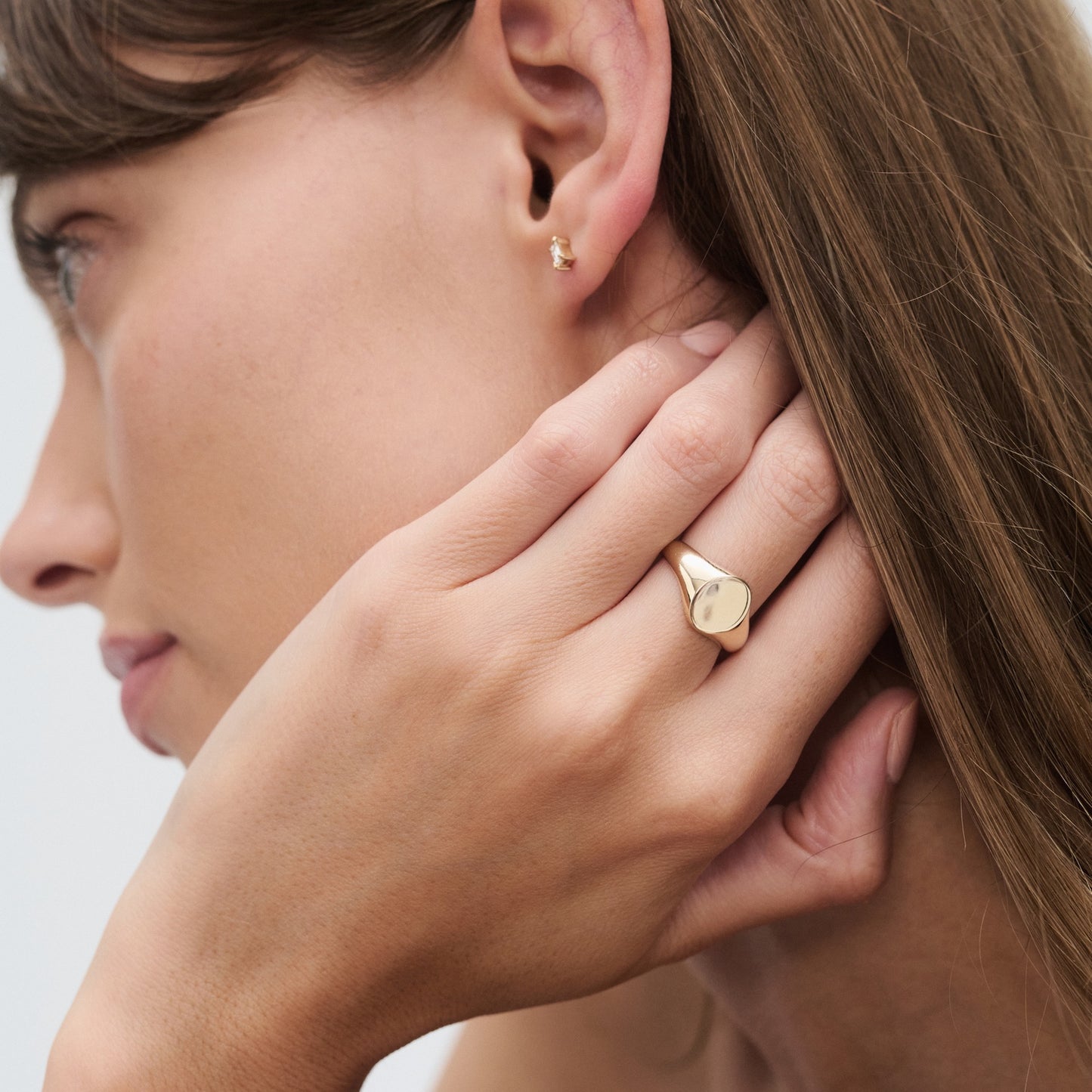 Woman wearing a gold ring and stud earring, close-up of her profile. Luxurious jewellery, elegant and minimalist design.