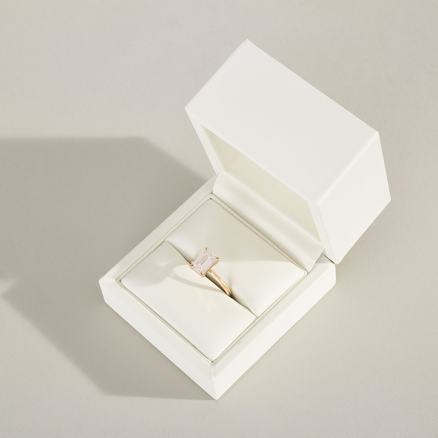 Diamond ring in an open white jewelry box on a light gray background