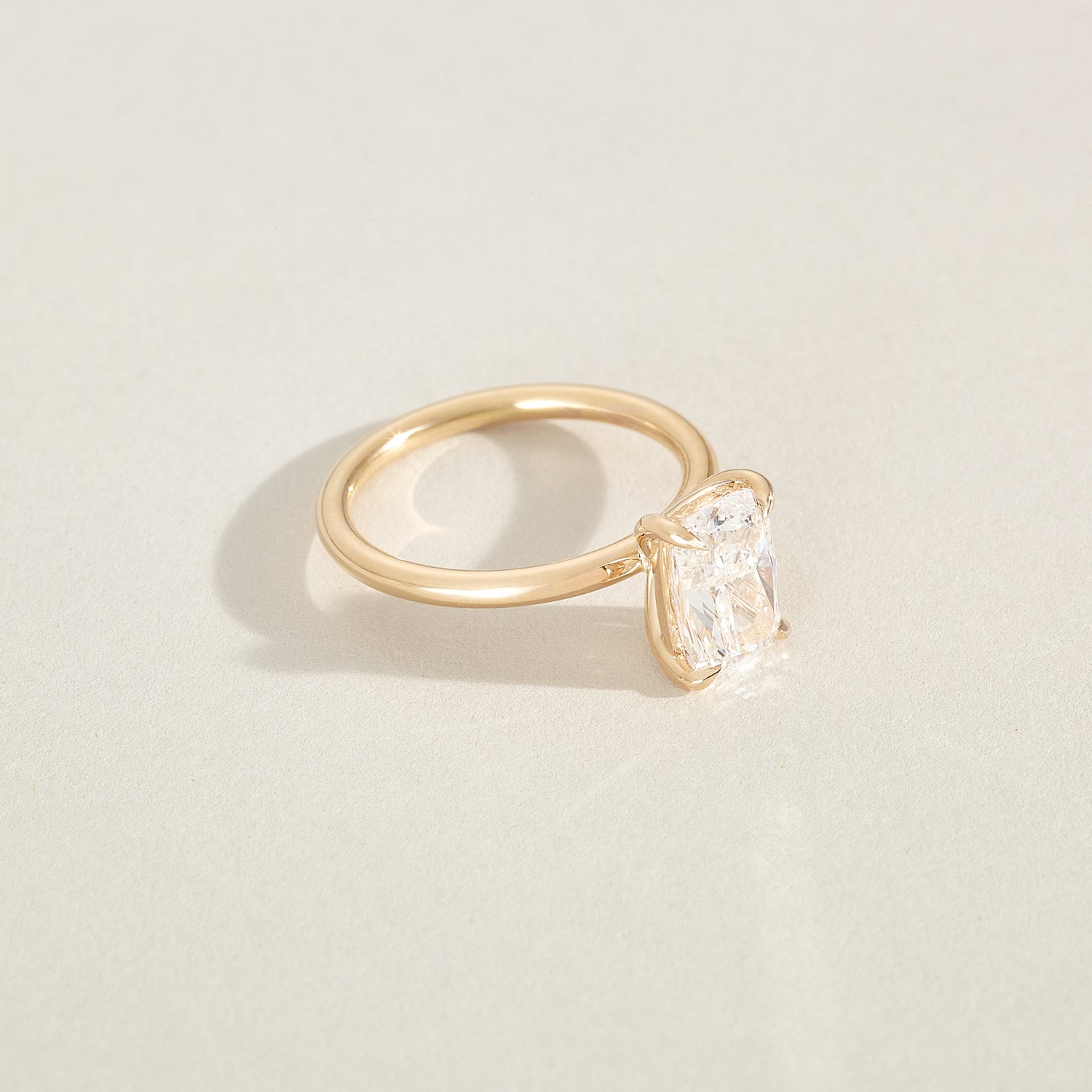 Gold ring with a cushion-shaped diamond on a light beige background