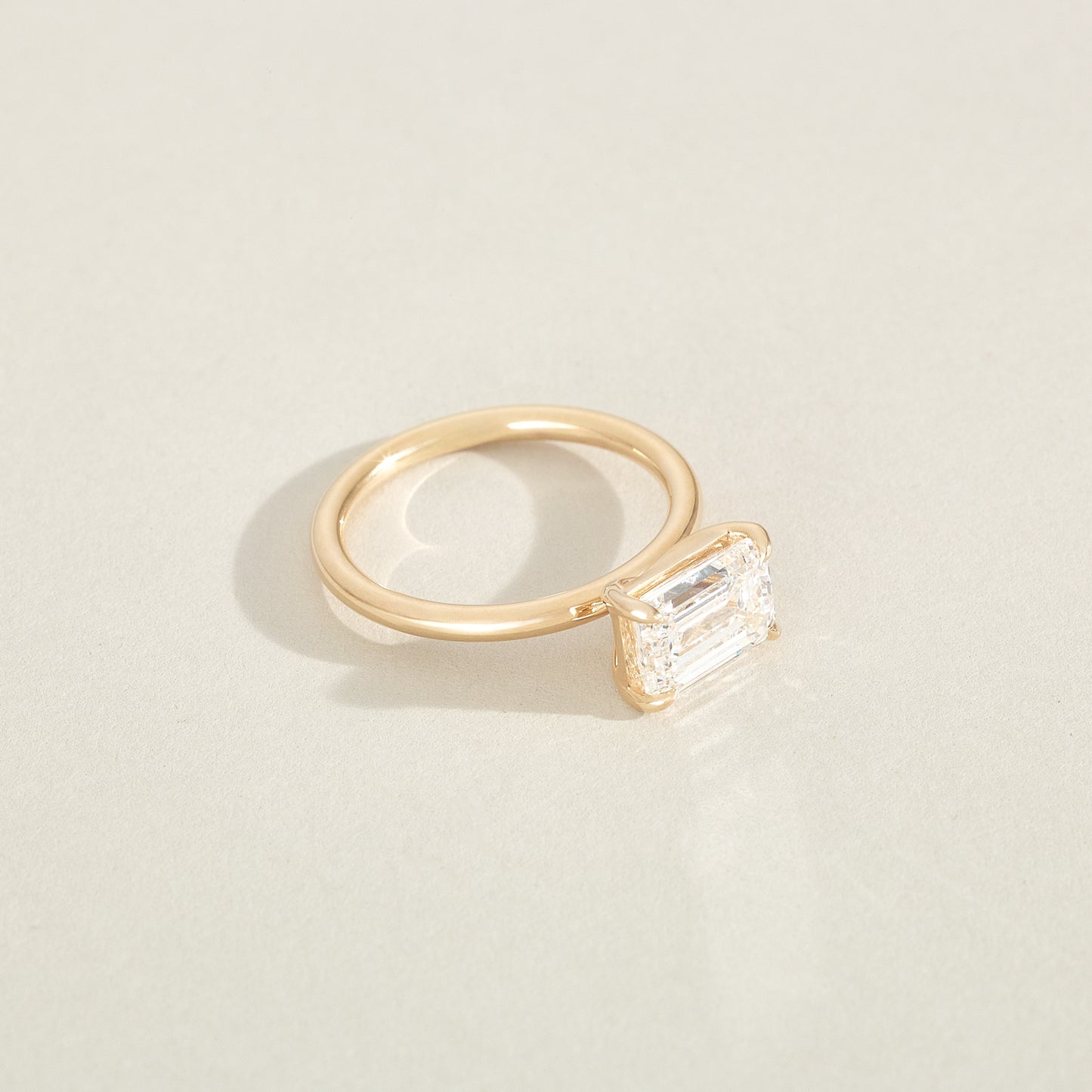 Gold ring with a rectangular diamond on a light beige background