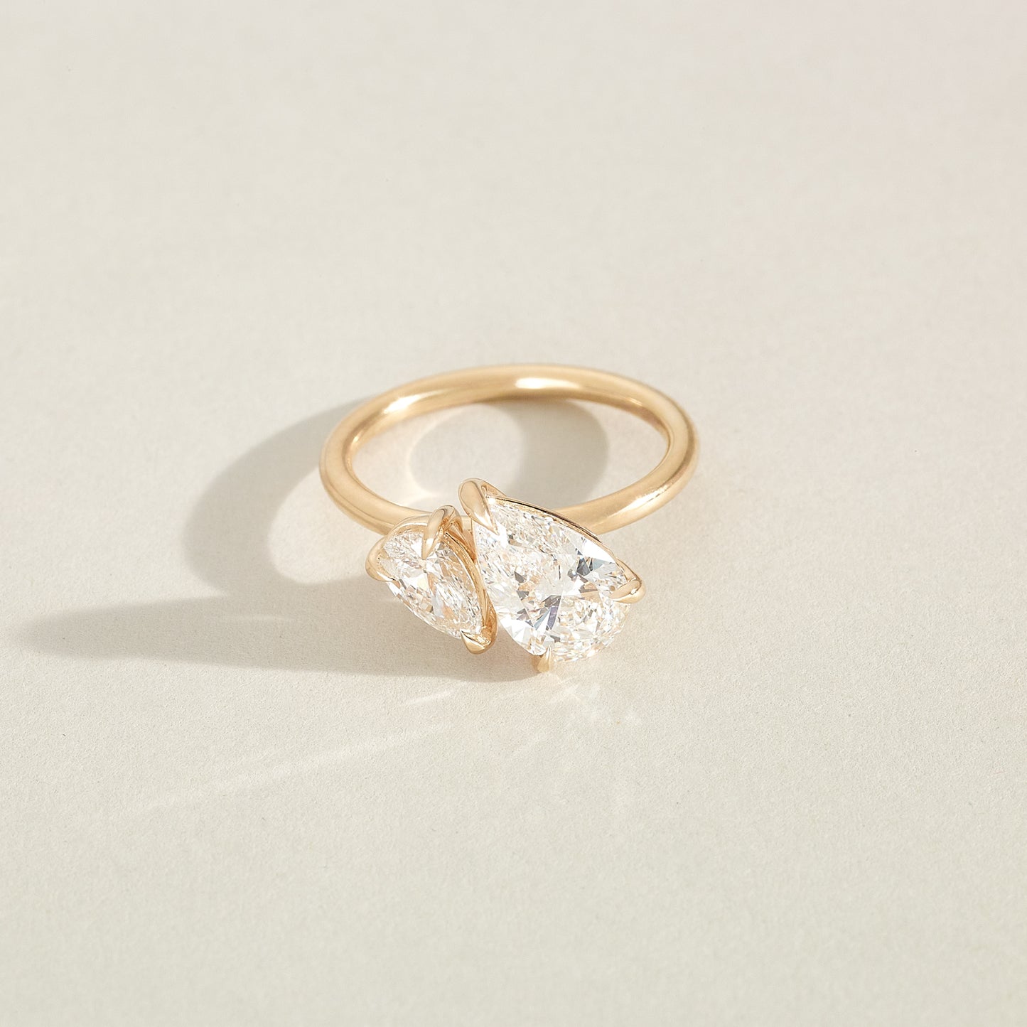 Gold ring with two pear-shaped diamonds on a light beige background