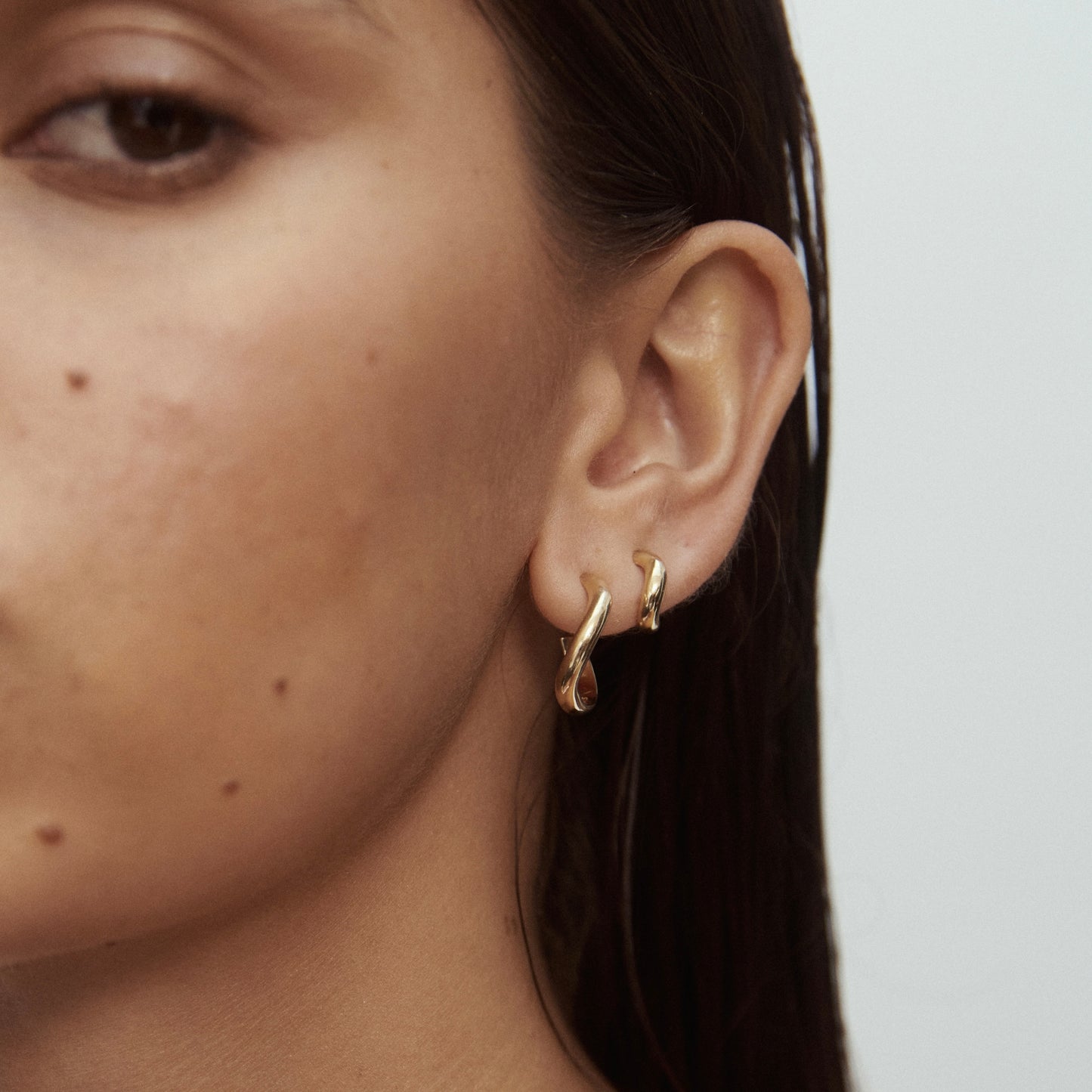 Close-up of a woman's ear wearing two elegant, gold twisted hoop earrings. Luxurious jewellery showcasing minimalistic design style.