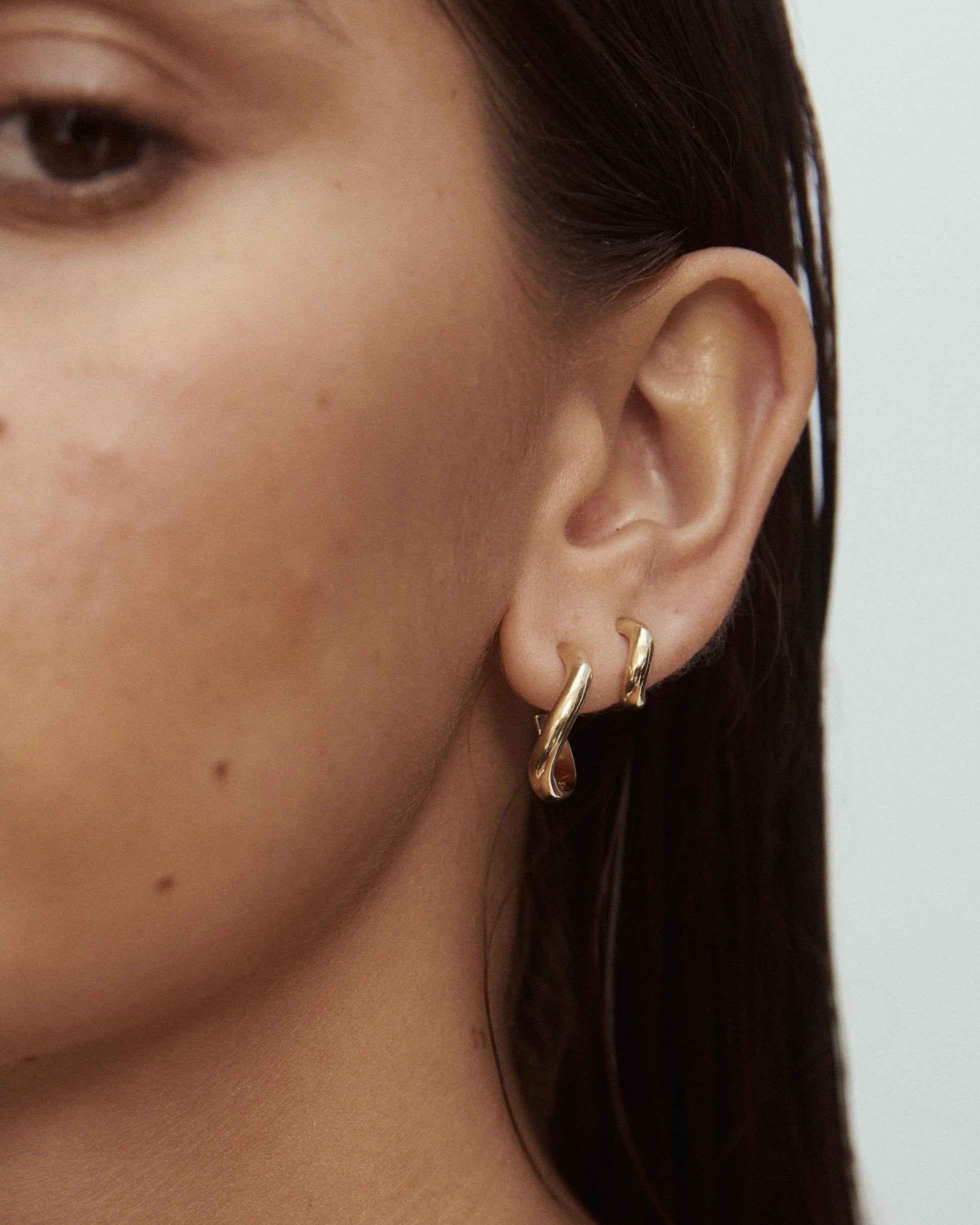Close-up of a person wearing gold hoop earrings with a neutral background