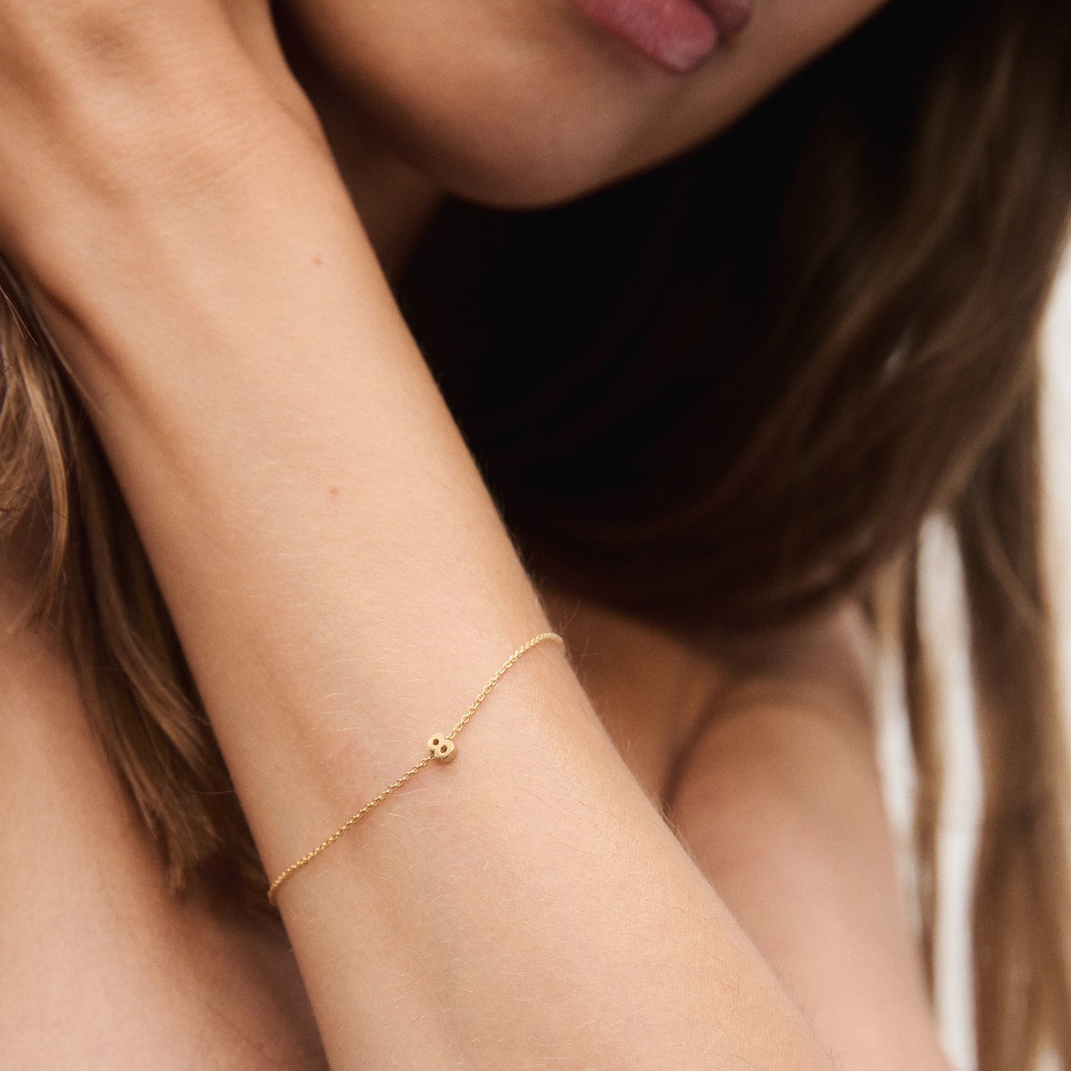 A woman wearing a delicate gold bracelet with a small bead, highlighting luxury jewellery on her wrist against a soft-focus background.