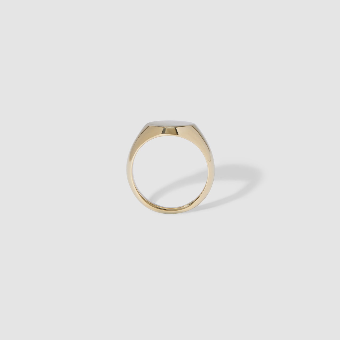 Gold signet ring with smooth, minimalist design on a light grey background, casting a soft shadow. Perfect for luxury jewellery lovers.