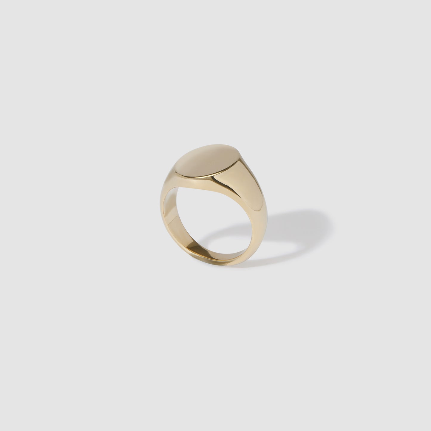 Gold signet ring on a white background, featuring a polished oval face and sleek band, casting a soft shadow. Perfect for luxury jewellery lovers.