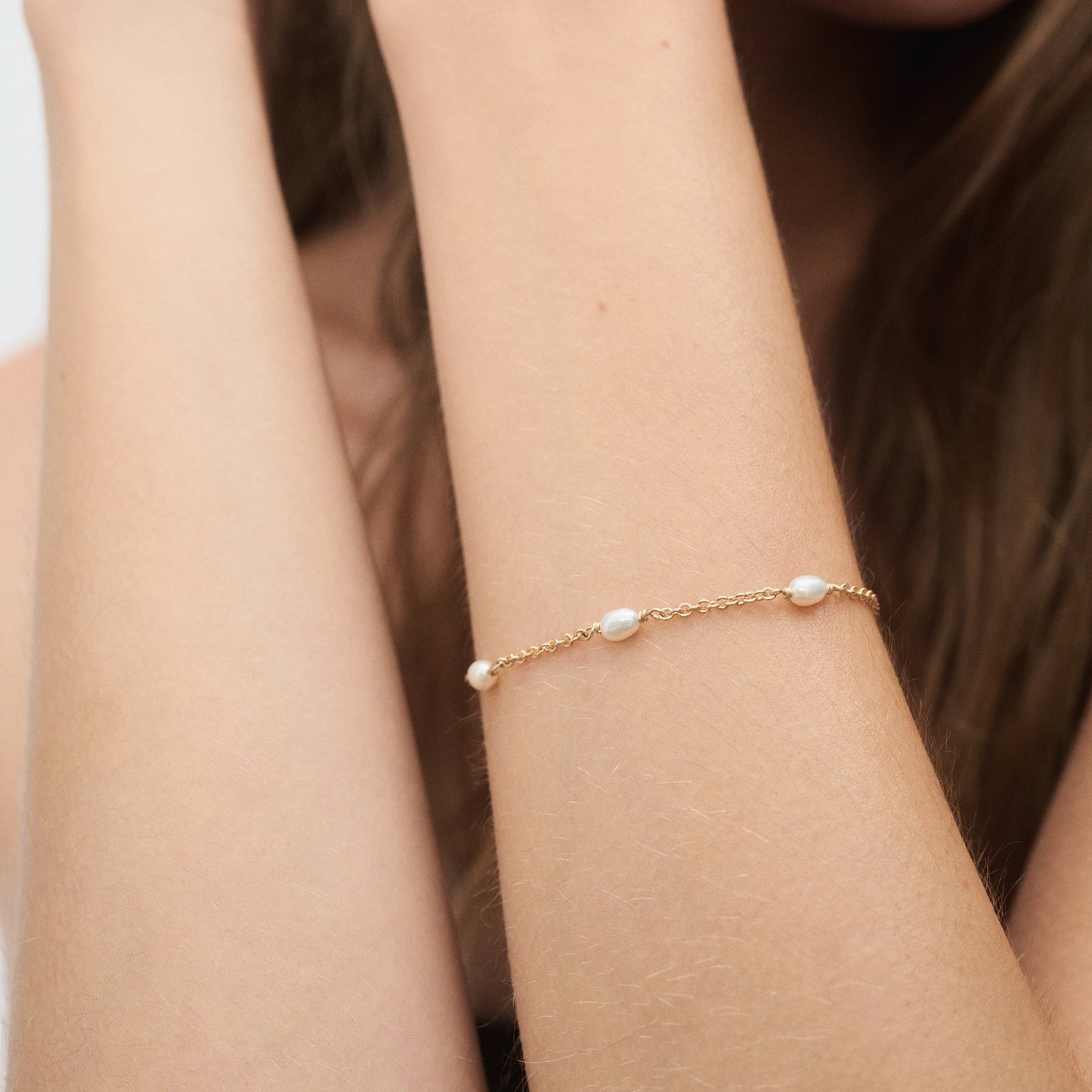 A gold bracelet with delicate pearls adorns a woman's wrist against a soft background, showcasing luxury jewellery elegance and style.