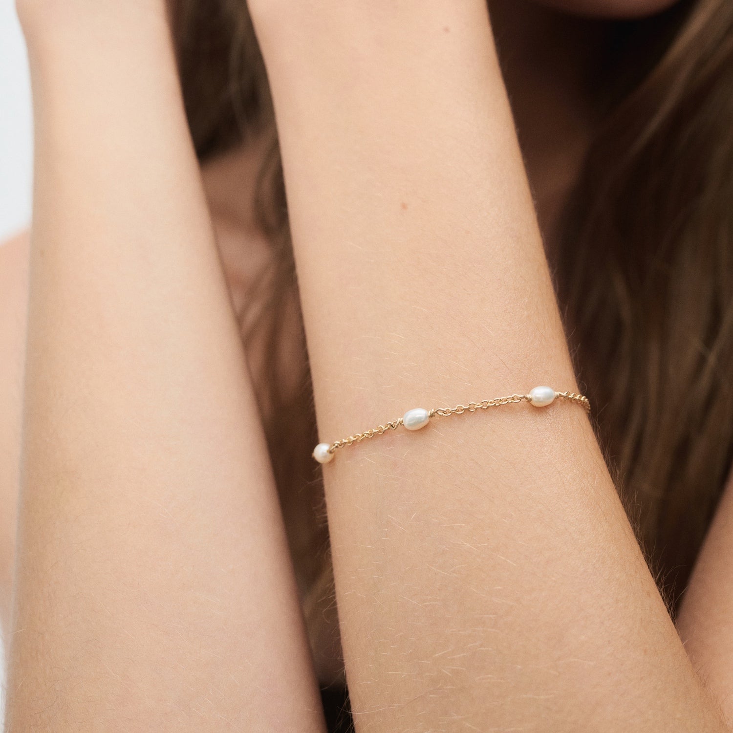 A gold bracelet with delicate pearls adorns a woman's wrist against a soft background, showcasing luxury jewellery elegance and style.