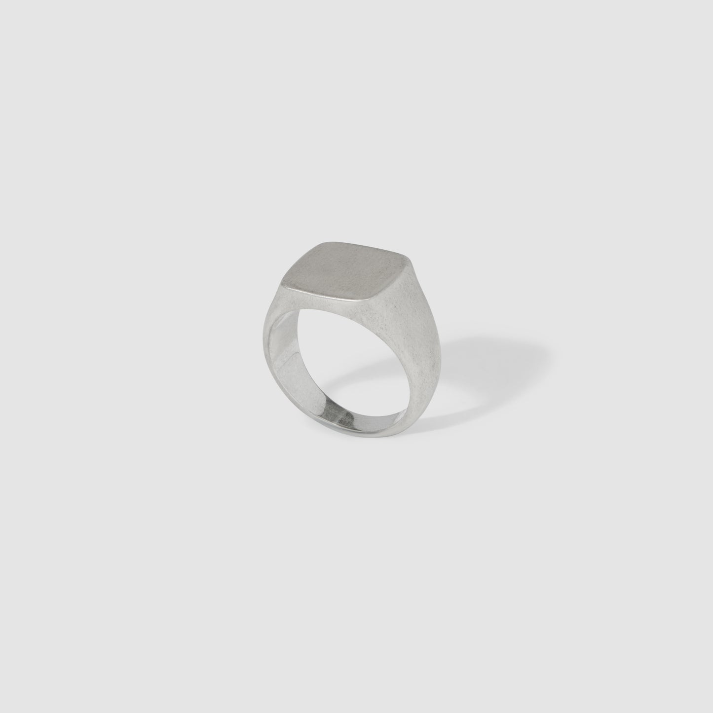 Silver signet ring with a smooth, rectangular face on a light grey background. Elegant and minimalist luxury jewellery.