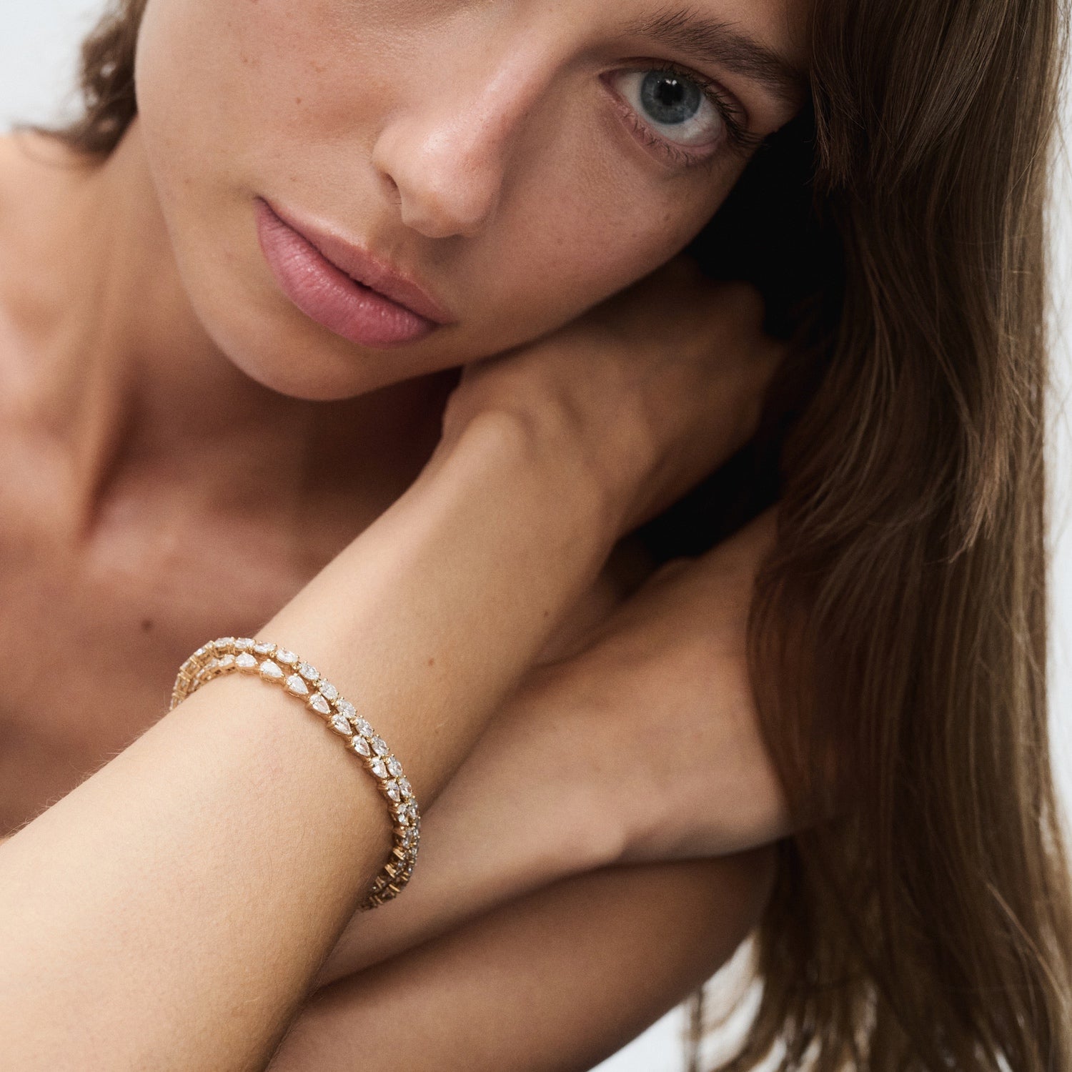 Woman wearing an elegant gold bracelet with diamond detailing, posing with her hand near her face, showcasing luxury jewellery.
