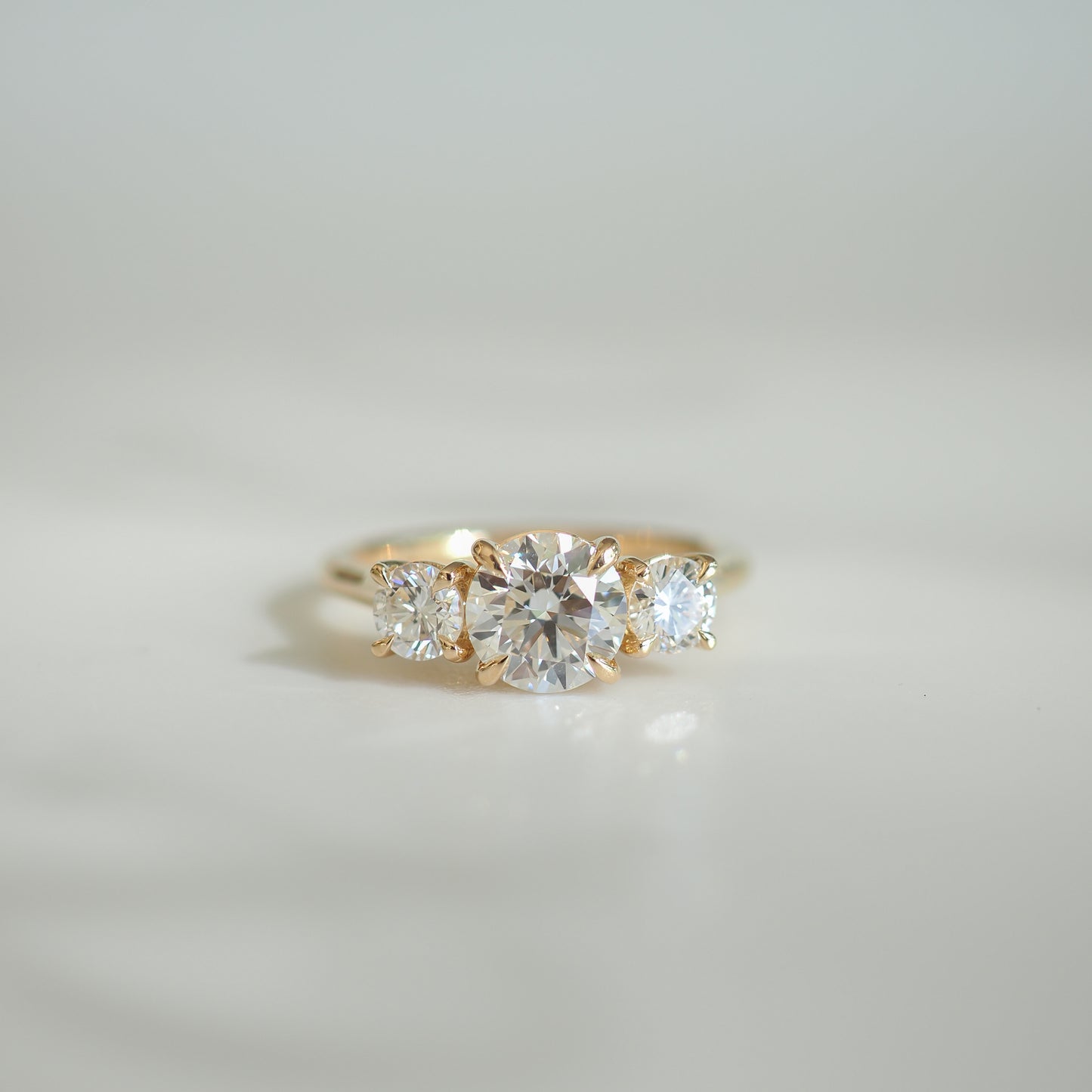 Elegant gold ring featuring four sparkling diamonds set in a symmetrical design against a soft, blurred background. Ideal for luxury jewellery lovers.