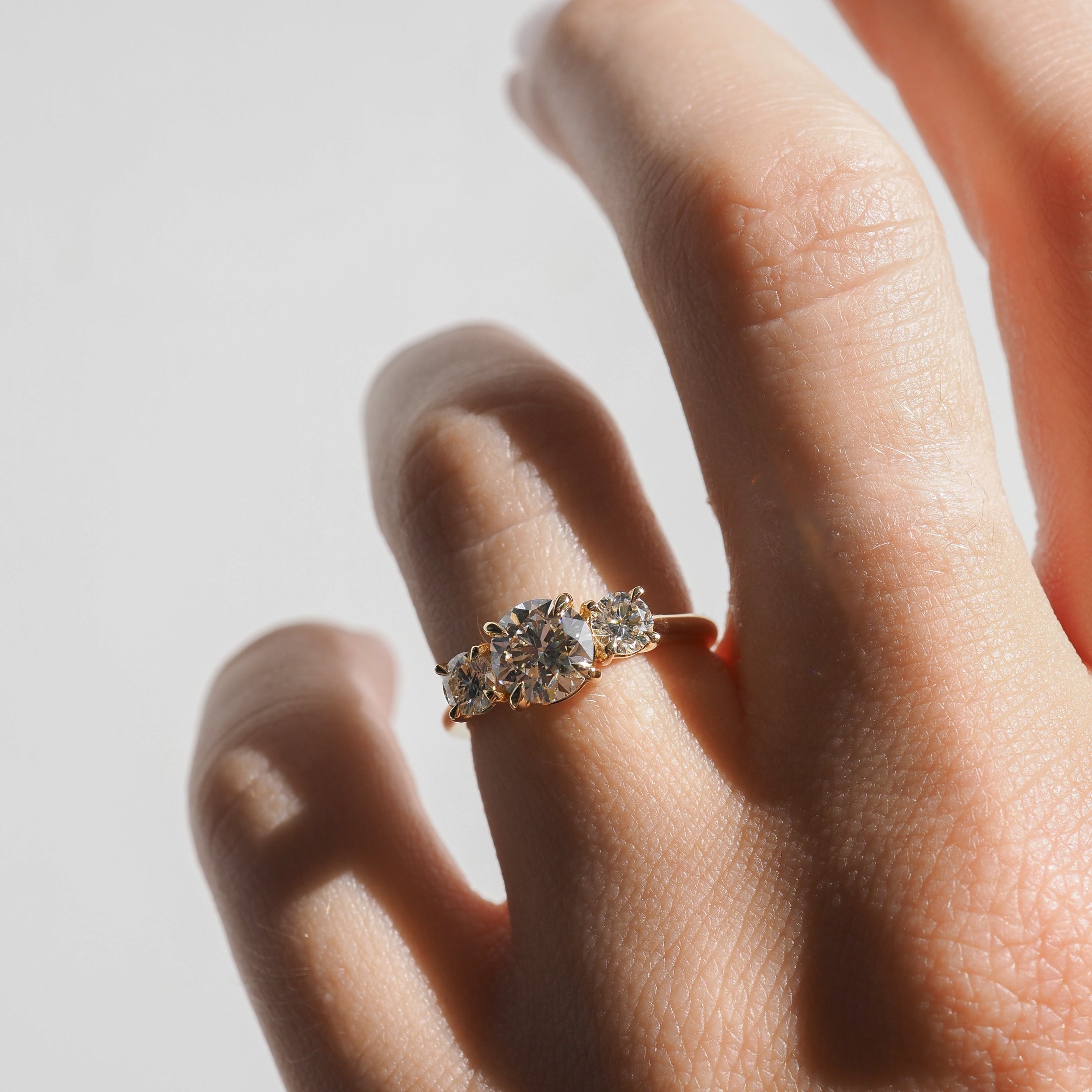 Hand with a three-stone diamond engagement ring; central round-cut diamond flanked by two smaller diamonds on a gold band.