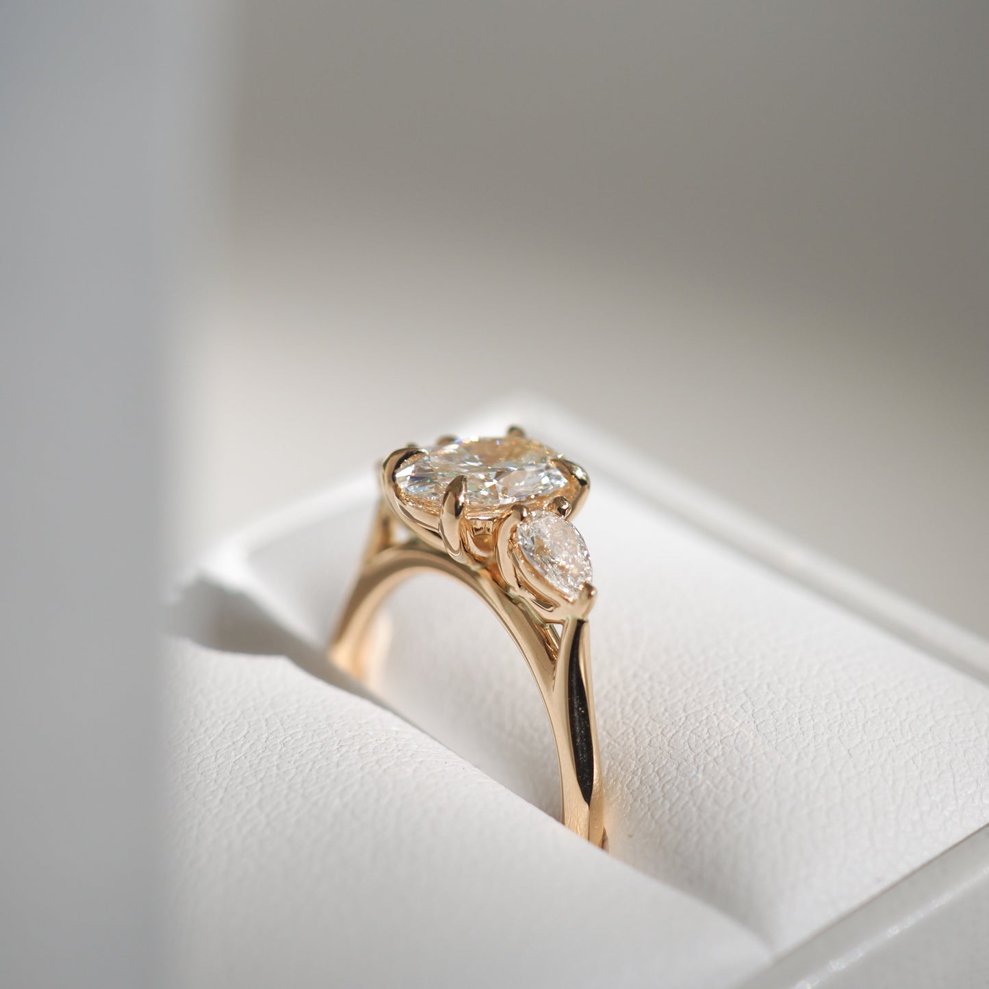 Gold ring with three oval diamonds set elegantly on a white cushion.