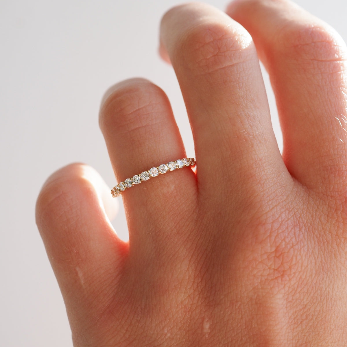 Hand wearing an elegant gold eternity band with sparkling round diamonds, showcasing luxury jewellery. Perfect for engagements or special occasions.