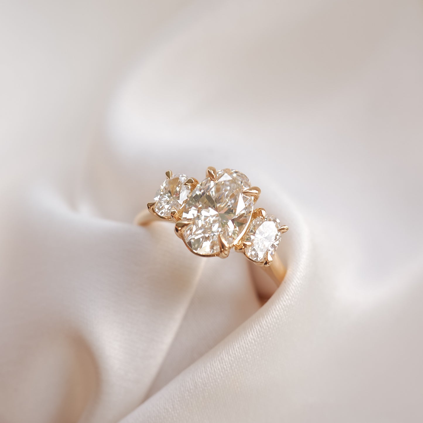 A gold ring with multiple large diamonds, elegantly placed on a soft, ivory fabric background, showcasing luxury jewellery.