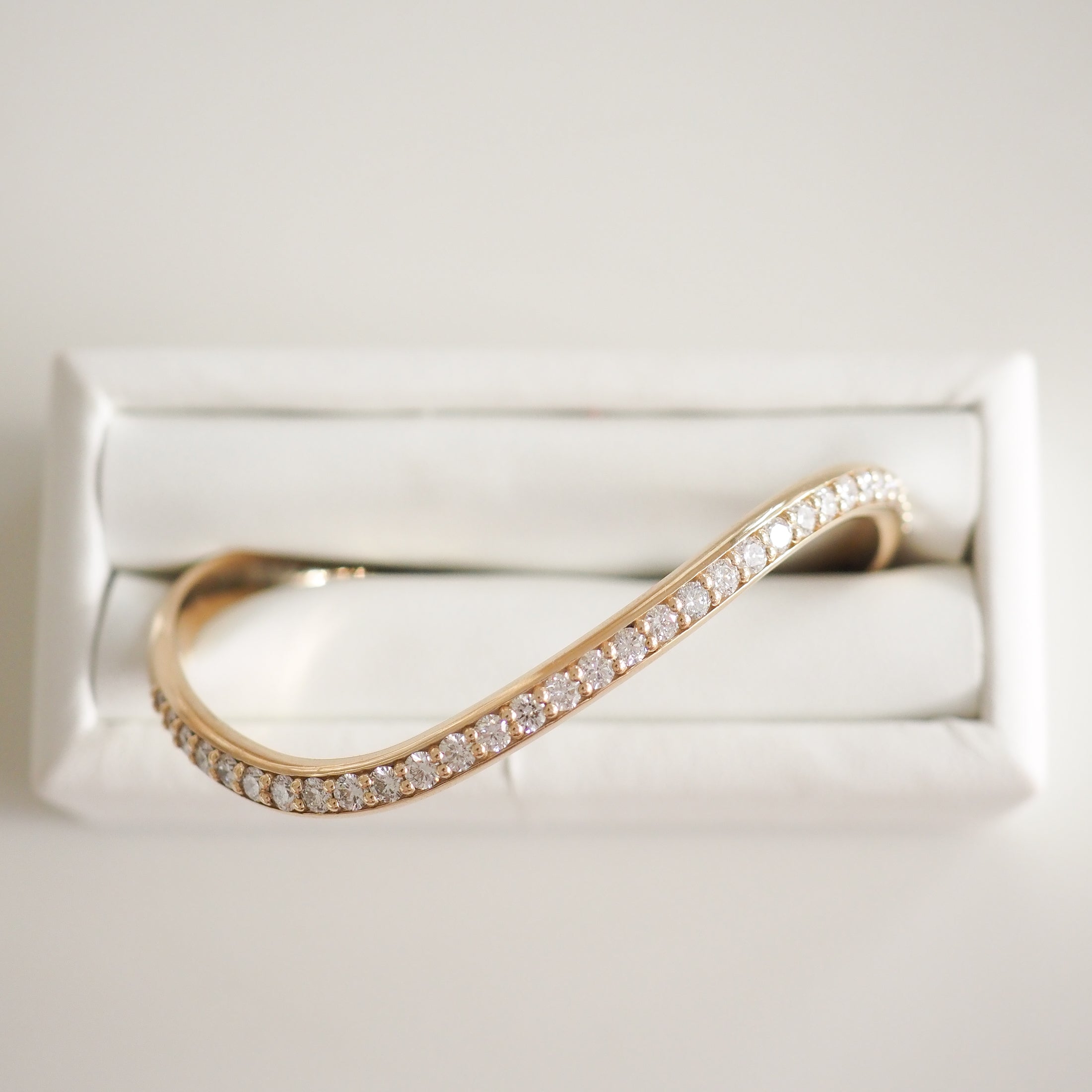 Elegant gold bracelet with curved design, encrusted with diamonds, displayed on a white cushioned box. Perfect for luxury jewellery enthusiasts.