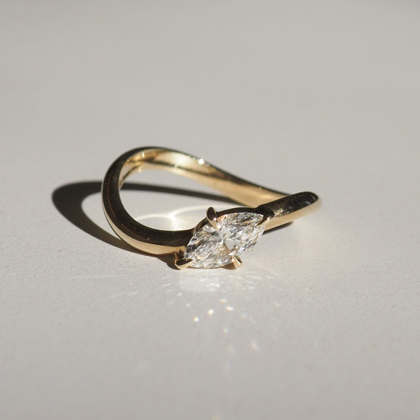 Gold ring with a marquise-cut diamond, elegantly curved band, casting a shadow on a white surface. Perfect for luxury jewellery lovers.