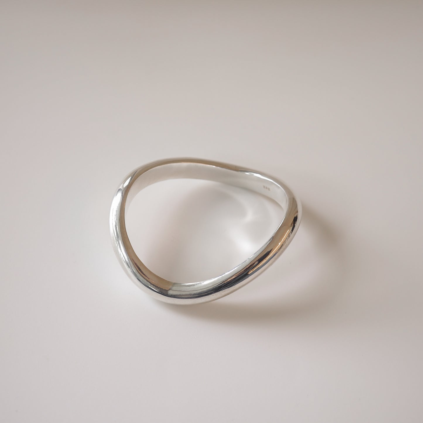 Elegant sterling silver bangle with a smooth, wavy design on a neutral backdrop. High-end handcrafted jewellery piece.