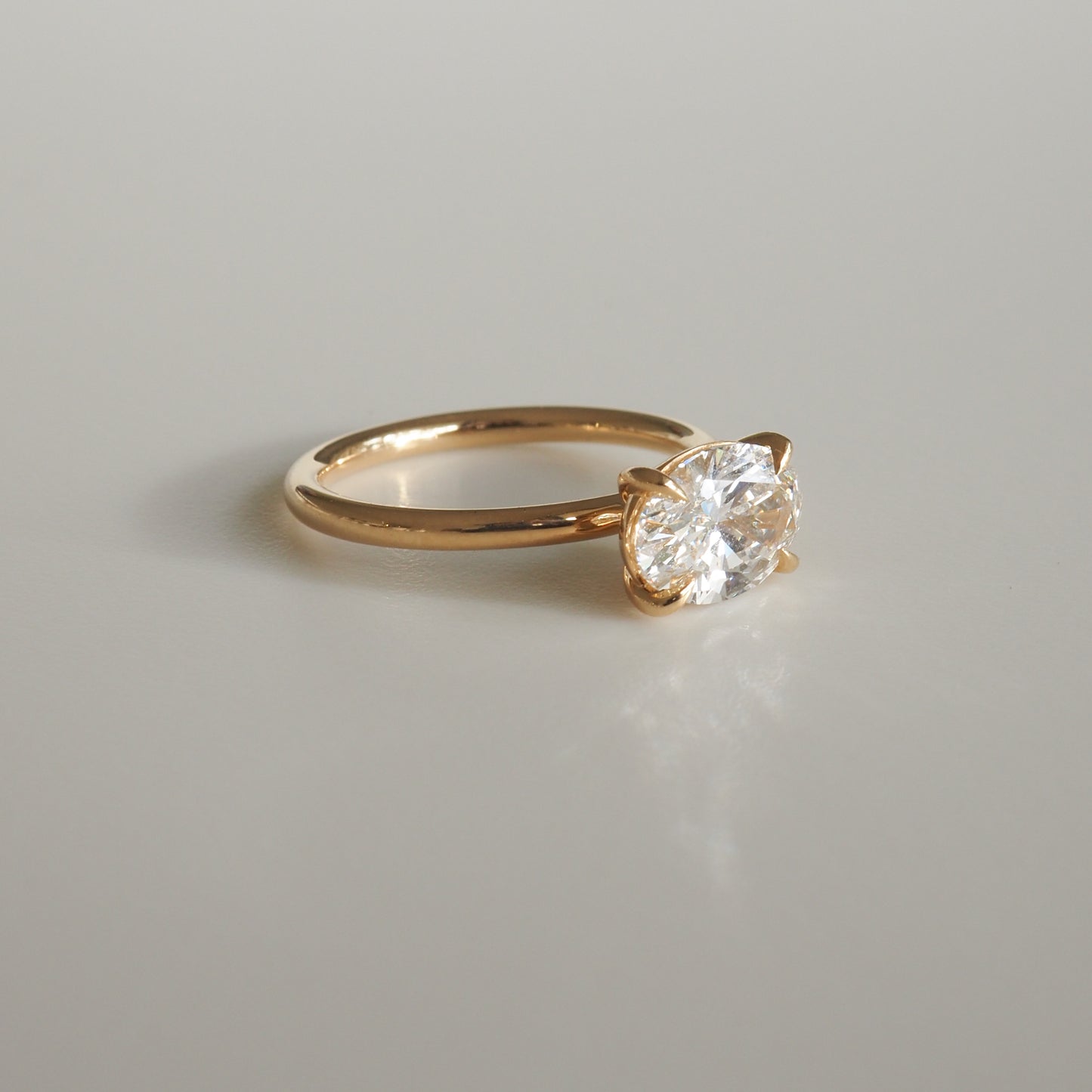 Gold ring with a large oval-cut clear gemstone, showcasing minimalist luxury jewellery design on a light grey background.