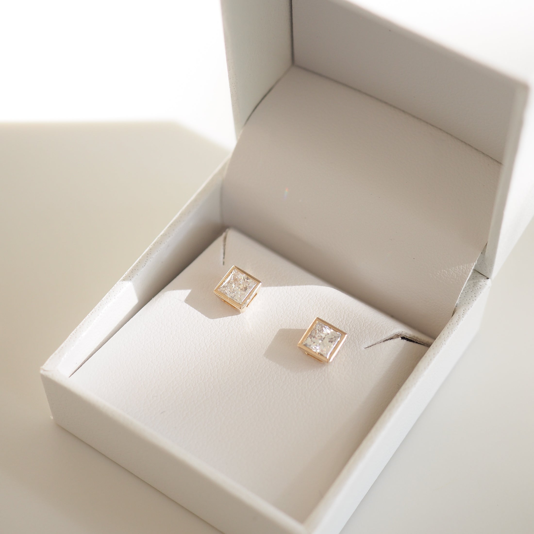 Square diamond stud earrings in a white jewellery box, capturing luxury shine and elegance. Perfect for high-end fashion and style.