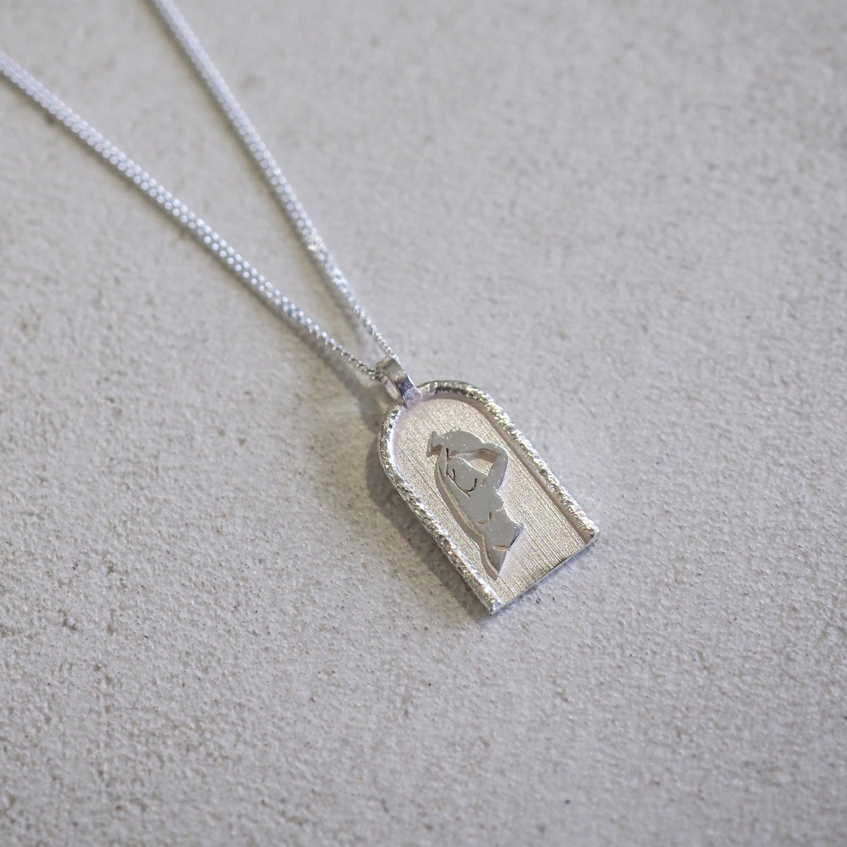 Silver pendant necklace with an arch-shaped design on a smooth beige surface, ideal for luxury jewellery enthusiasts.