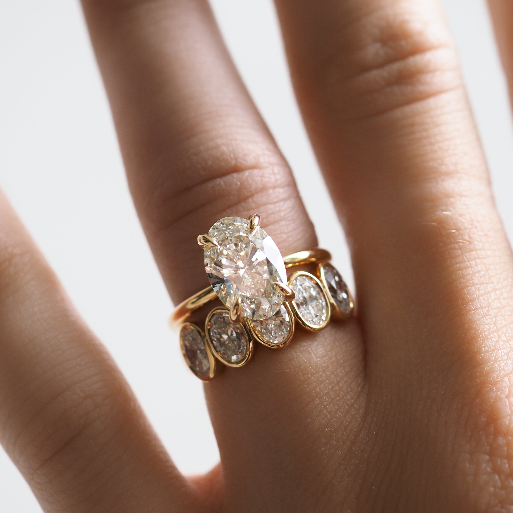 Close-up of a hand wearing a gold oval-cut diamond engagement ring and a matching band with multiple smaller diamonds, showcasing luxury jewellery.