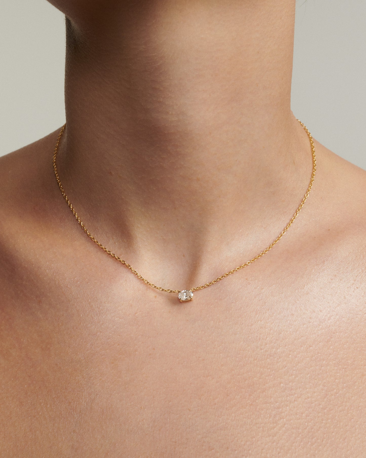 Gold necklace with a diamond pendant on a person's neck against a neutral background
