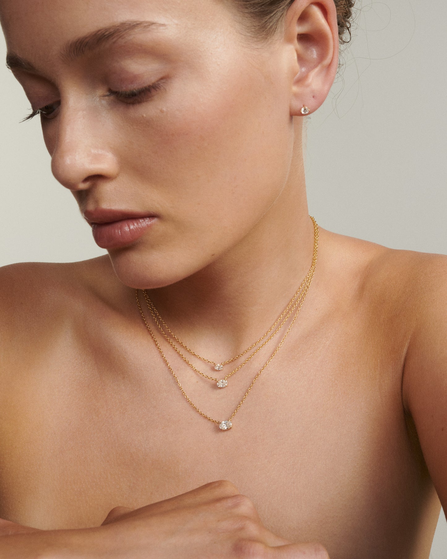 Close-up of a woman wearing gold necklaces and earrings on a neutral background