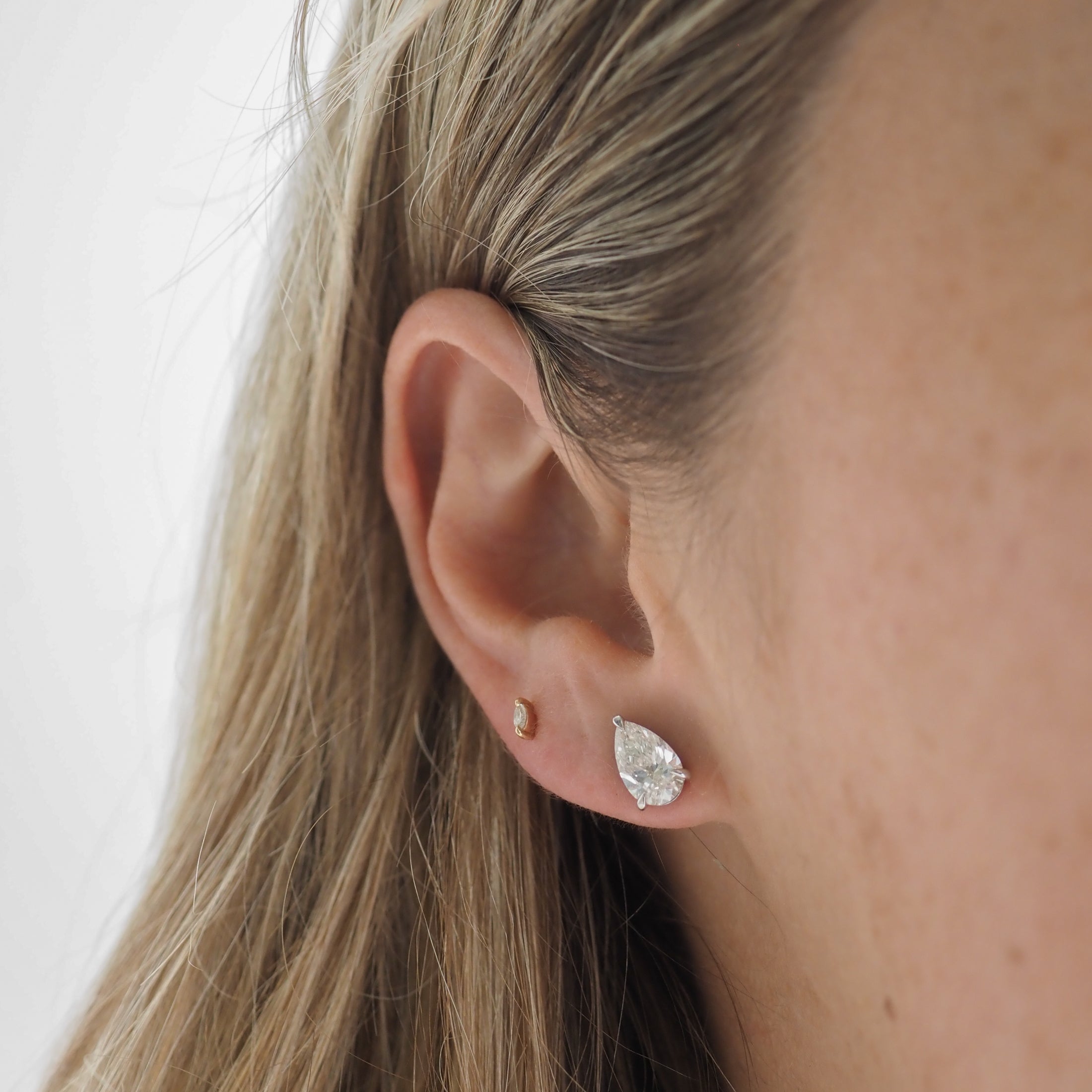Close-up of a woman's ear wearing a teardrop diamond stud earring and a small gold earring, showcasing luxury jewellery detail.