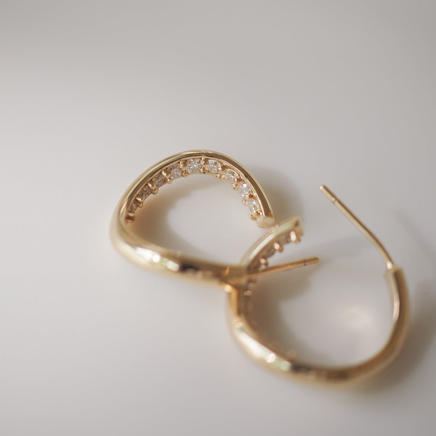 Gold hoop earrings with embedded diamonds, elegantly displayed on a smooth, light background. Luxurious, high-end jewellery.