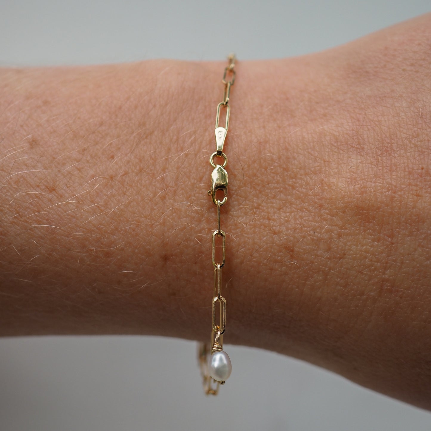 Elegant gold chain bracelet with a single pearl accent on a wrist, showcasing luxurious jewellery design and craftsmanship.