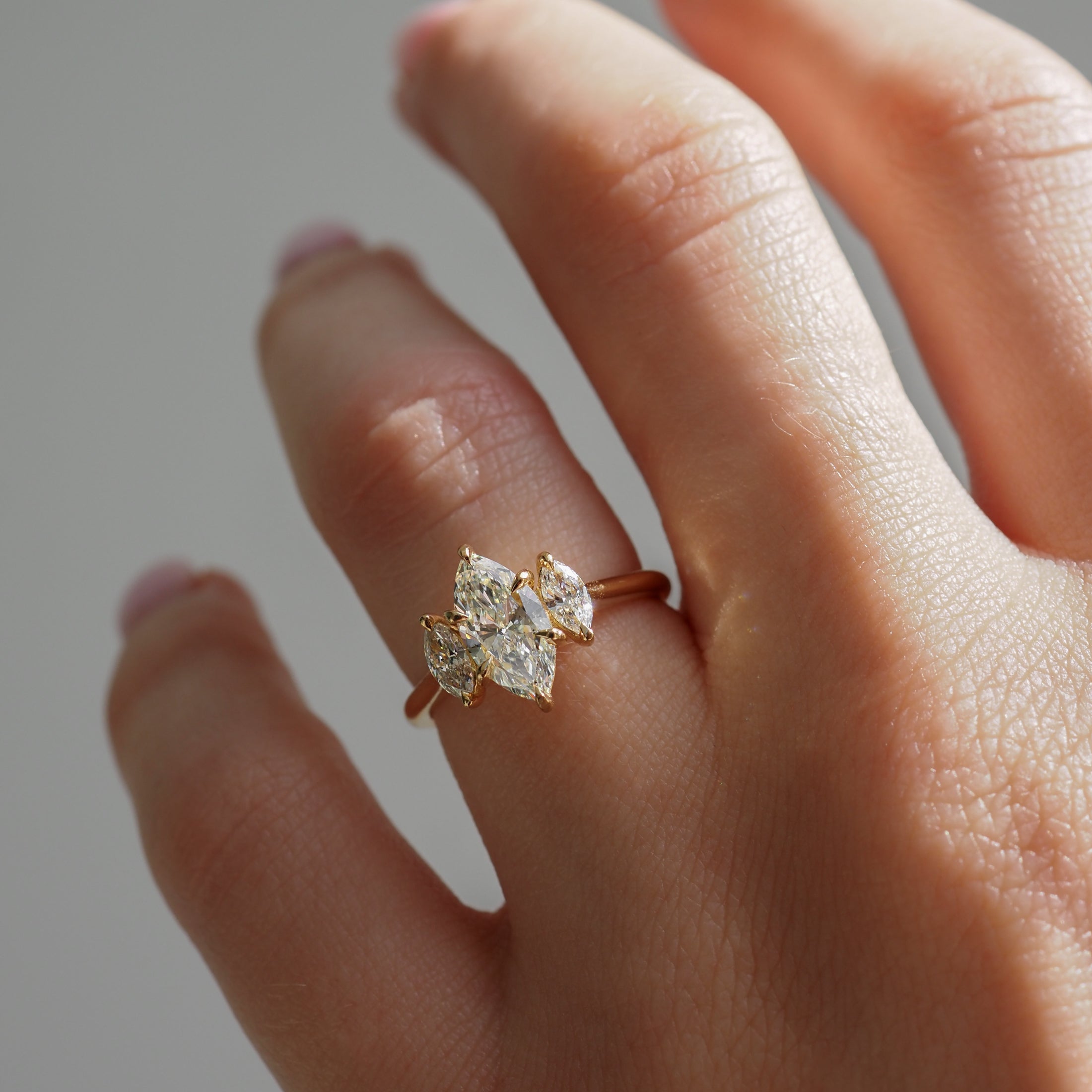 Elegant gold ring with three marquise diamonds on a hand, showcasing luxury jewellery design.