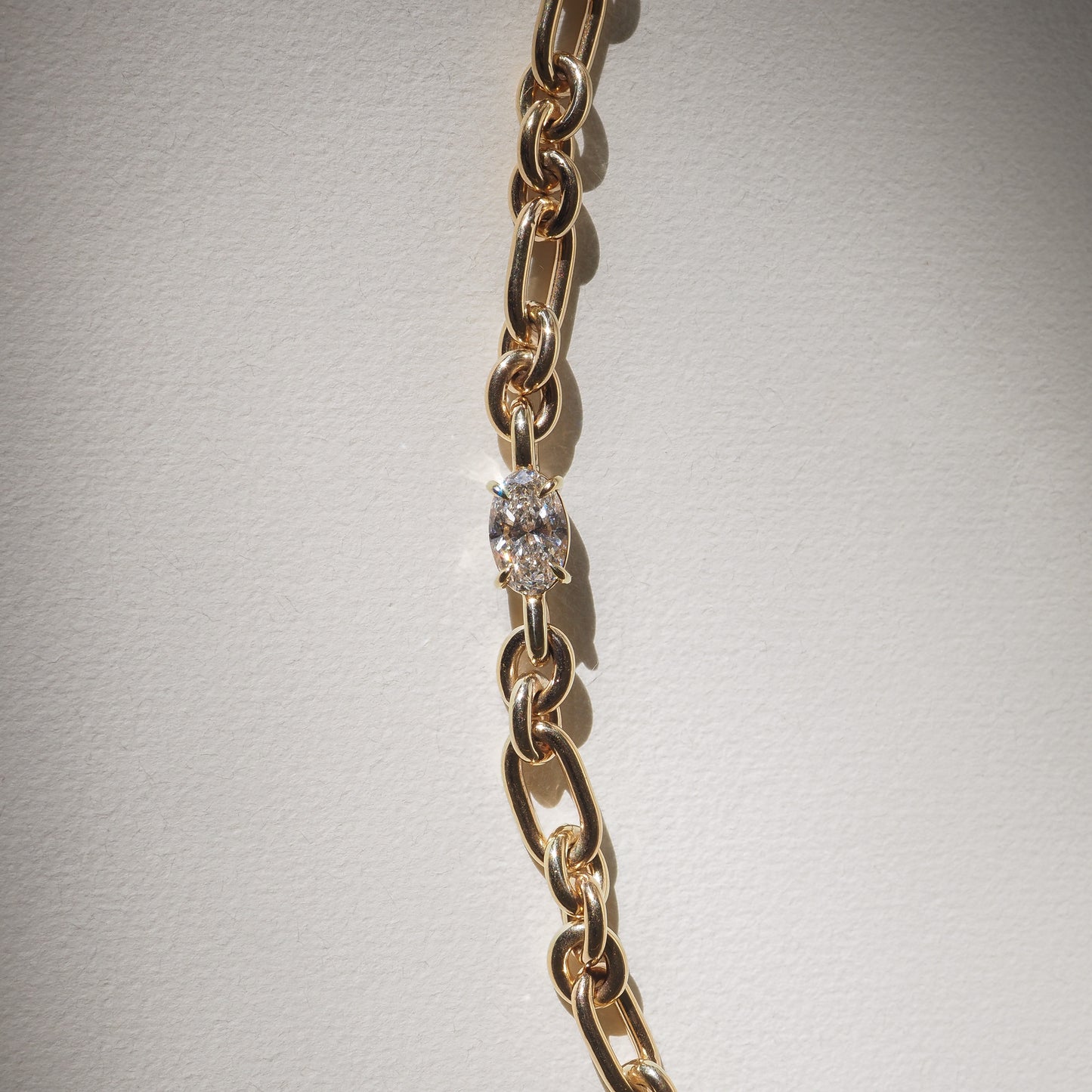 Gold chain with oval diamond link, elegant and minimalist luxury jewellery on a light background.
