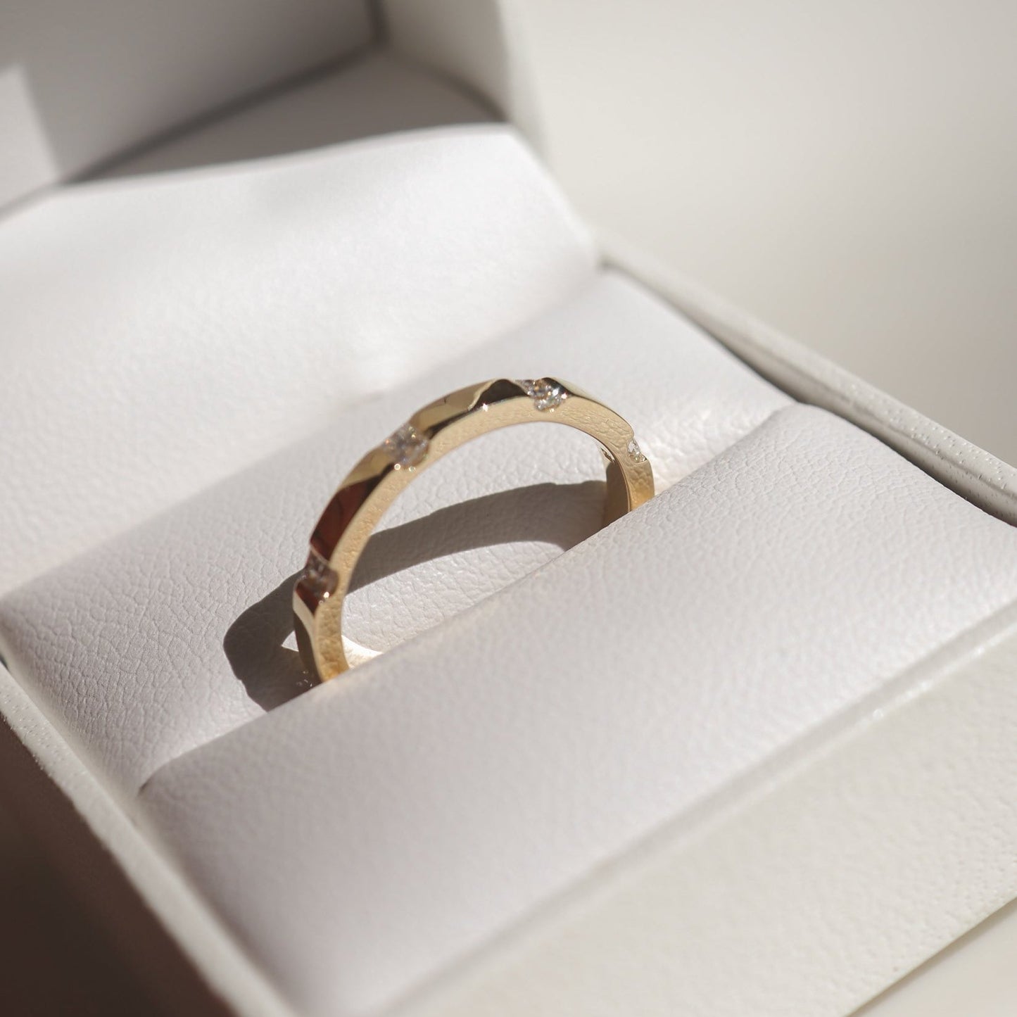 Gold ring with geometric design set with small diamonds, showcased in a white jewellery box, highlighting luxury craftsmanship.