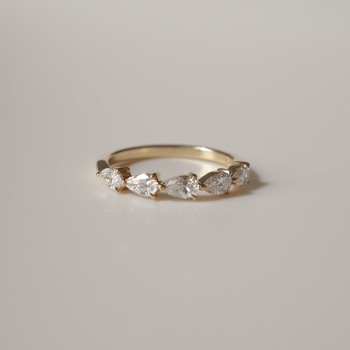 Gold ring with five pear-shaped diamonds set in a row, reflecting elegant luxury jewellery design on a neutral background.